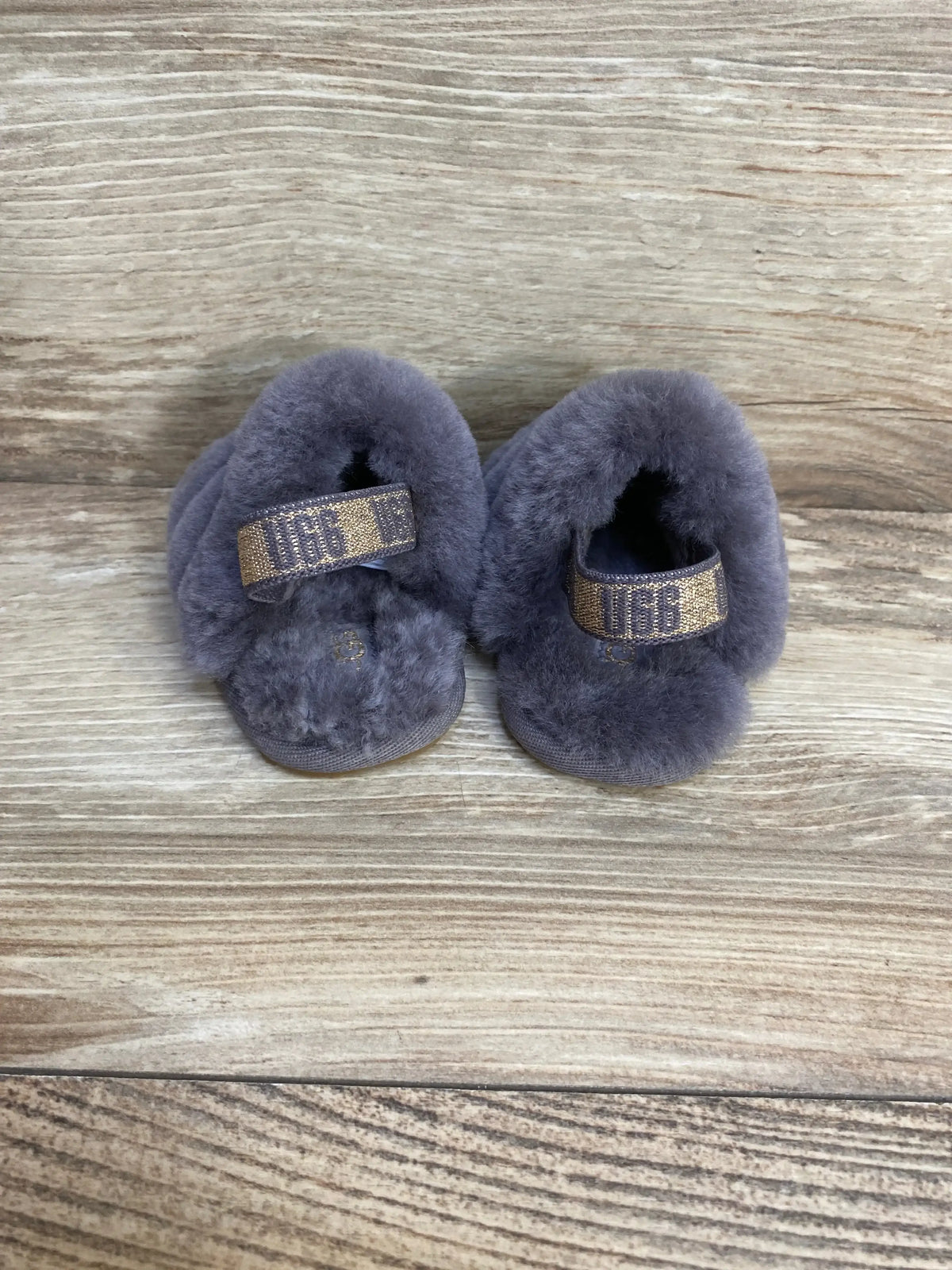 Top view of UGG Fluff Yeah toddler slides in grey showcasing soft sheepskin uppers and elastic heel straps on a wood background