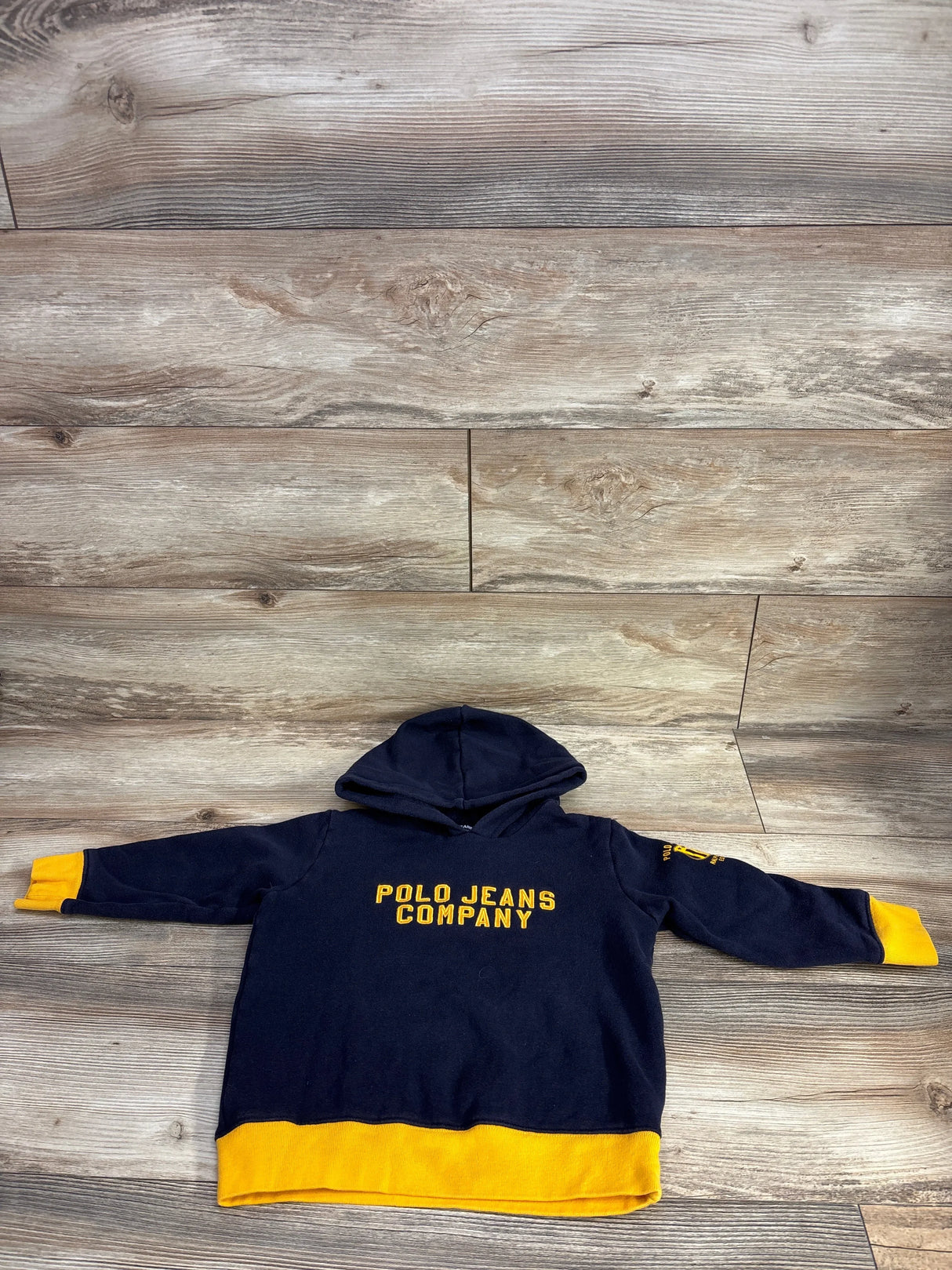 Navy blue kids hoodie with yellow accents and Polo Jeans Company text, laid on wood background