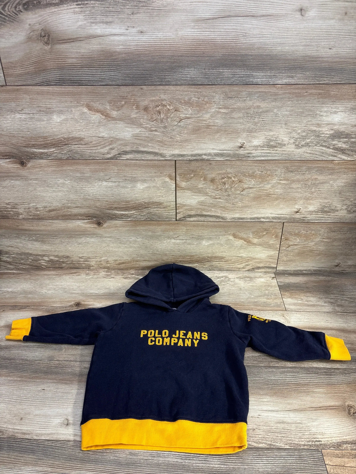 Navy blue kids hoodie with yellow accents and Polo Jeans Company text, laid on wood background