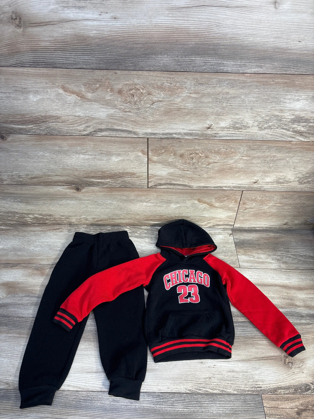 Top view of black two piece sweatshirt and joggers set showcasing red sleeves and Chicago 23 design on a wood floor