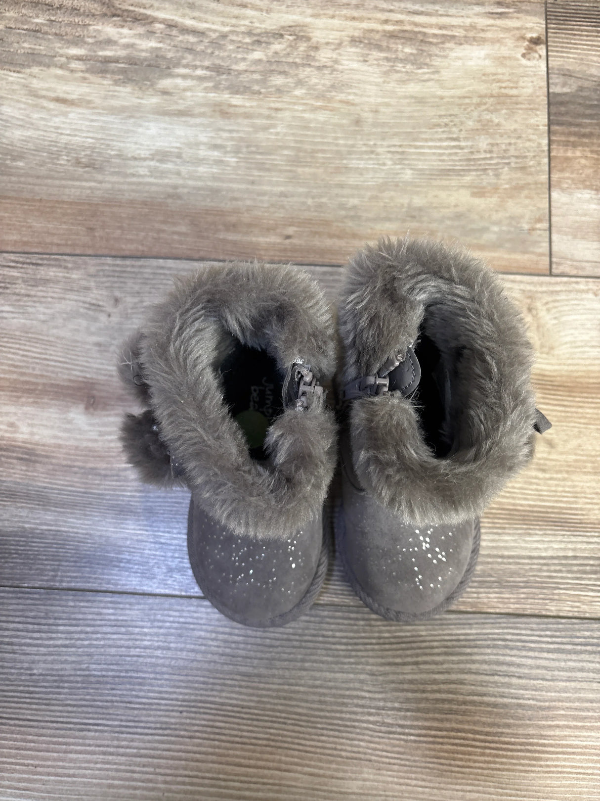 Top-down view of Jumping Beans Coco Easy Zip boots showcasing grey faux-fur cuffs, glitter-speckled toes, and side zippers on a wood floor