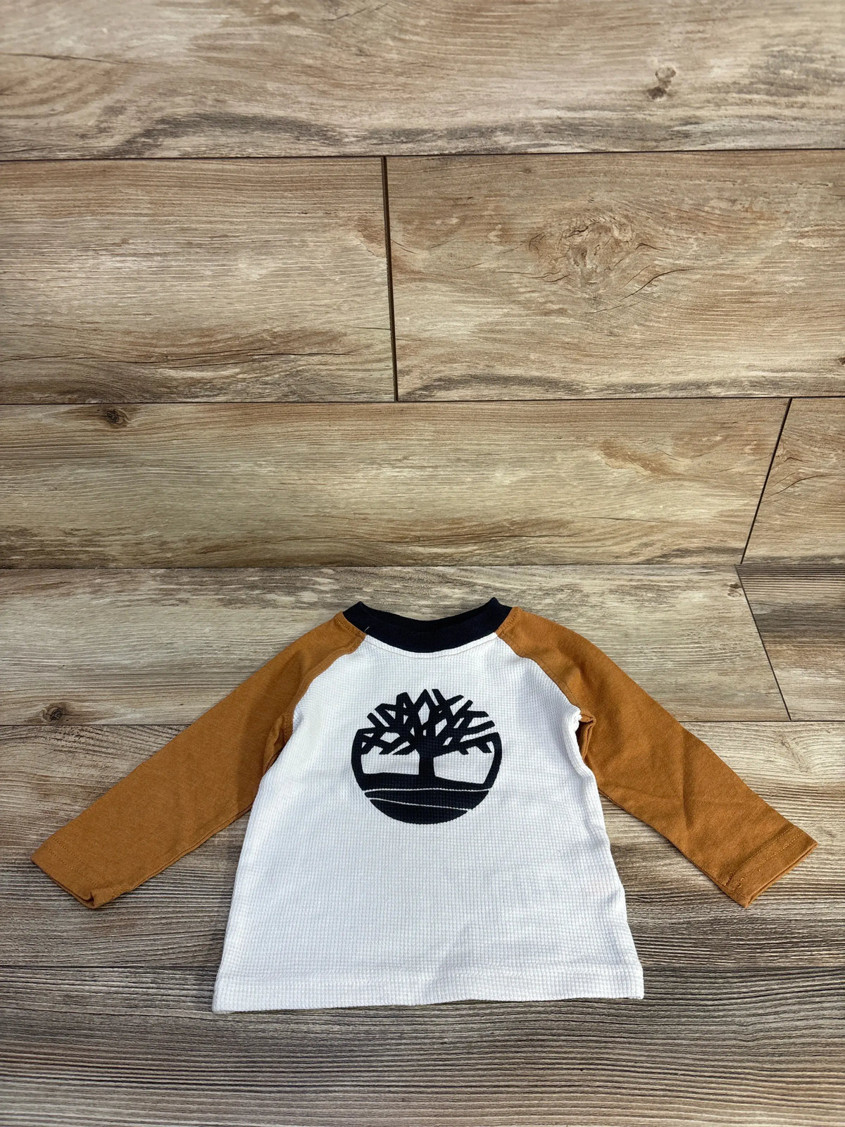 Front view of Timberland waffle knit shirt in tan, size 12 months, showcasing textured knit and tree logo on wood floor