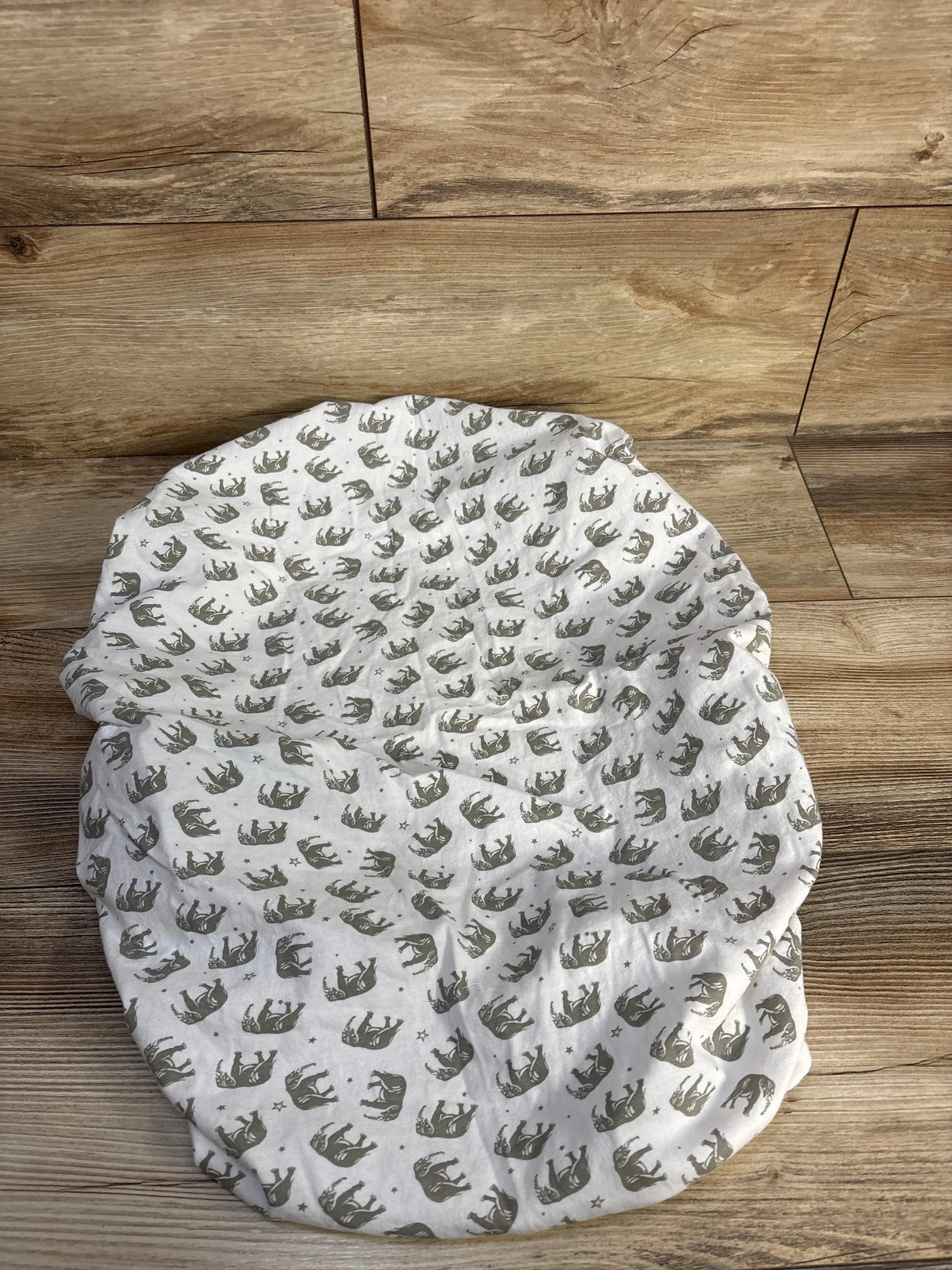 Top-down view of Bublo Baby fitted bassinet sheet showing gray elephant print and elastic fitted edge on wooden floor background