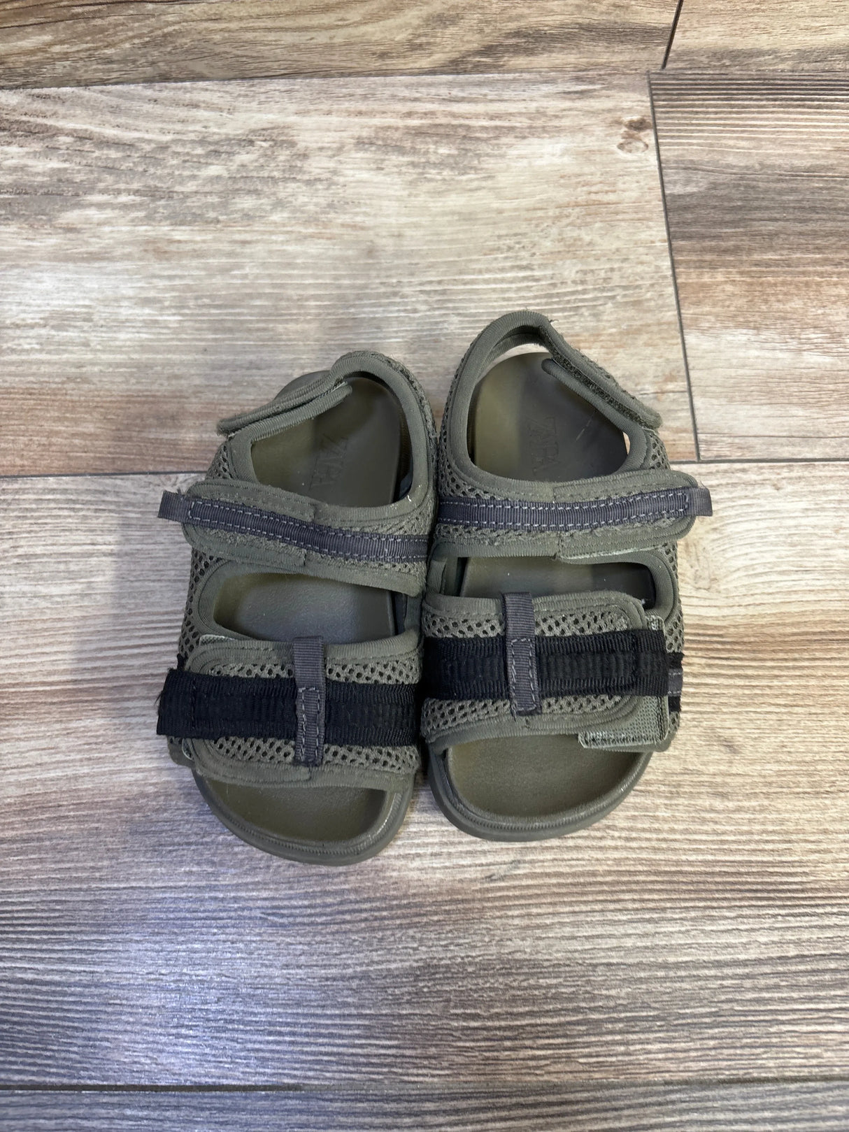 Top-down view of Zara scuba toddler sandals in olive green, size 7C, showing two adjustable Velcro straps and mesh upper on wood floor