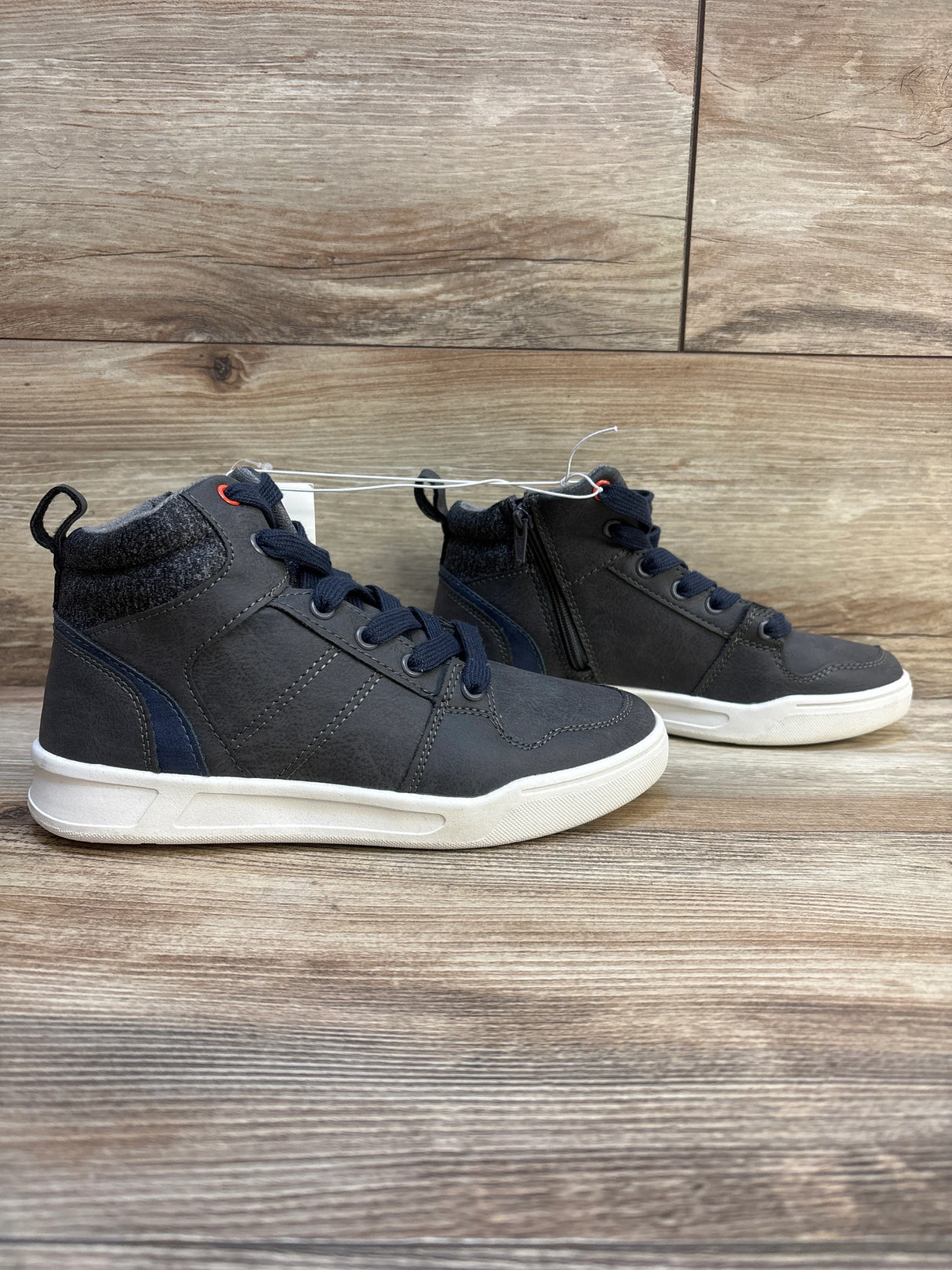 Kids' dark gray high top sneakers with white soles and navy laces on wood floor
