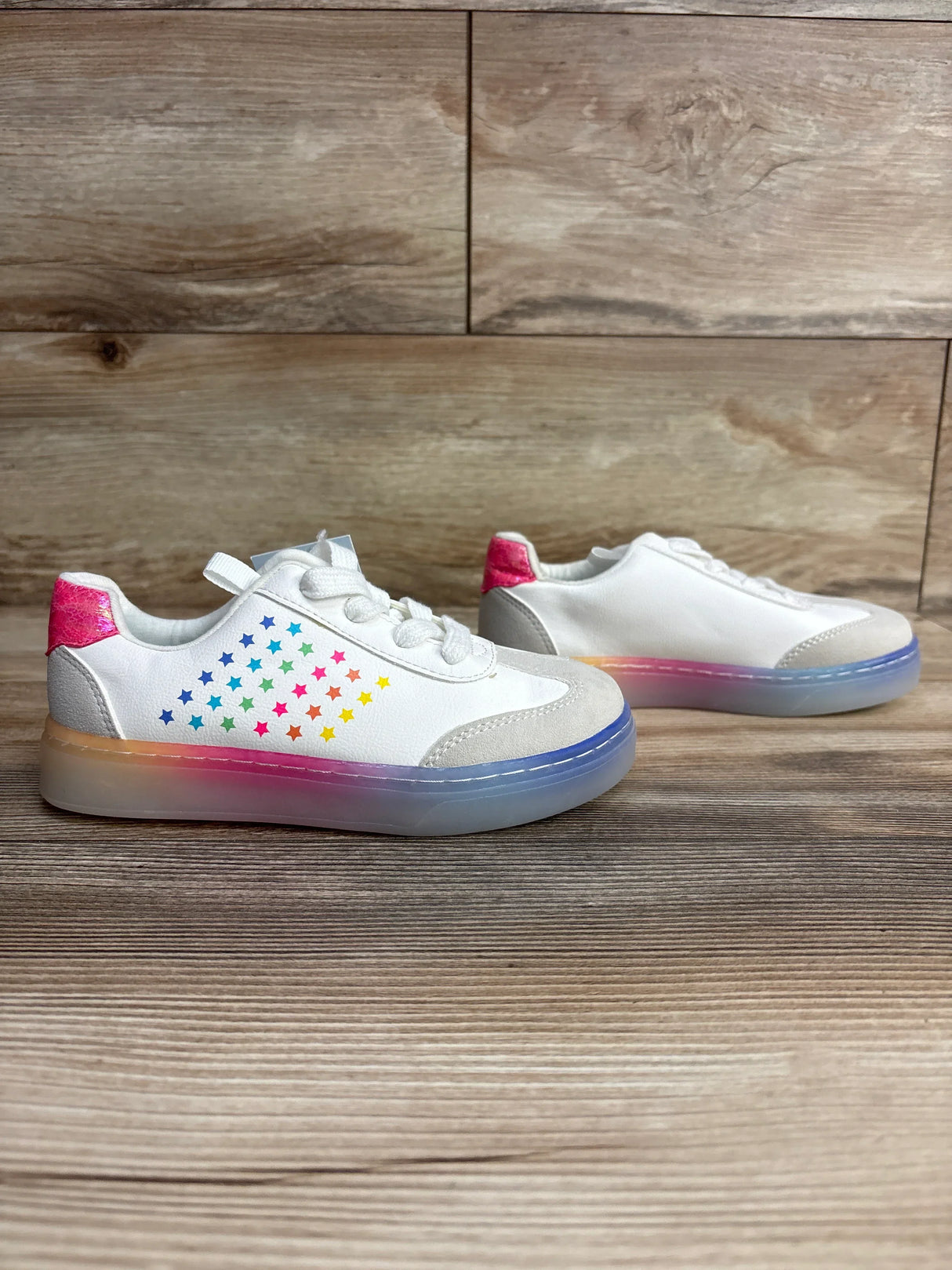 Side view of Cat & Jack Kira kids sneakers size 13C showing rainbow star pattern, pink heel tab, and translucent ombre sole on wood floor