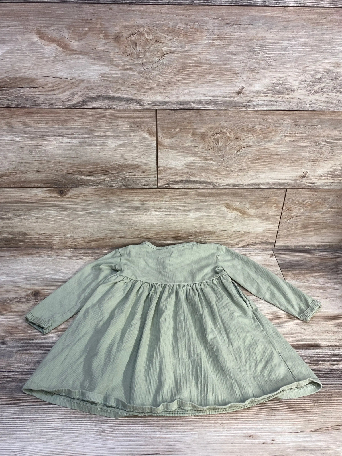 Flat lay of green long-sleeve Henley toddler dress (3T) showing gathered skirt and crinkled texture on wood background