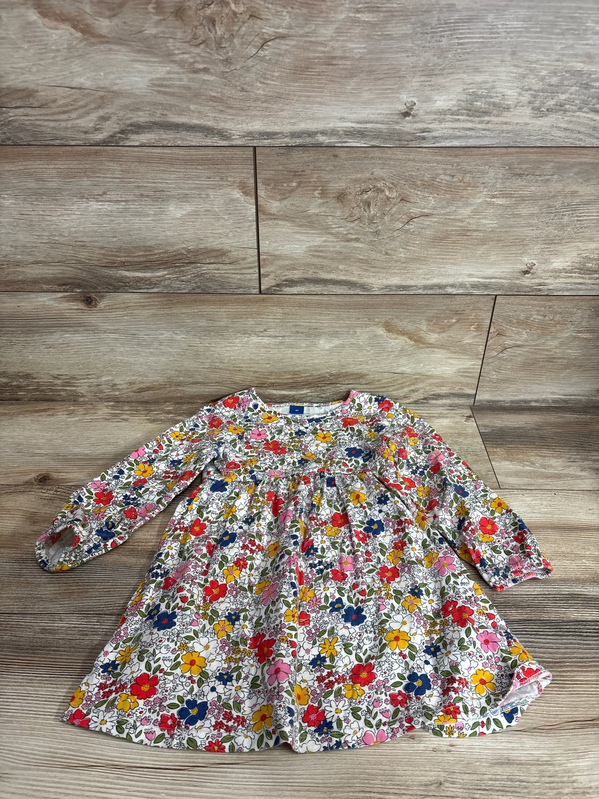 Flat lay of girl's white long-sleeve Old Navy floral dress showing gathered waist and elastic cuffs on wood floor background