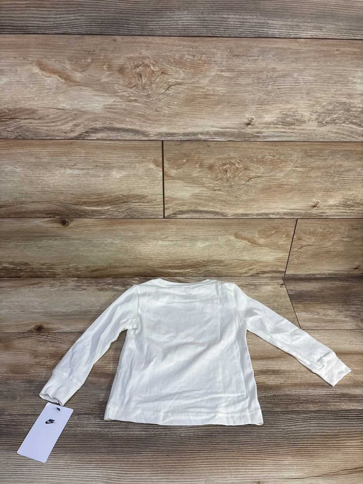 Back view of white Nike long sleeve toddler shirt (2T) laid flat on wood floor with visible Nike tag
