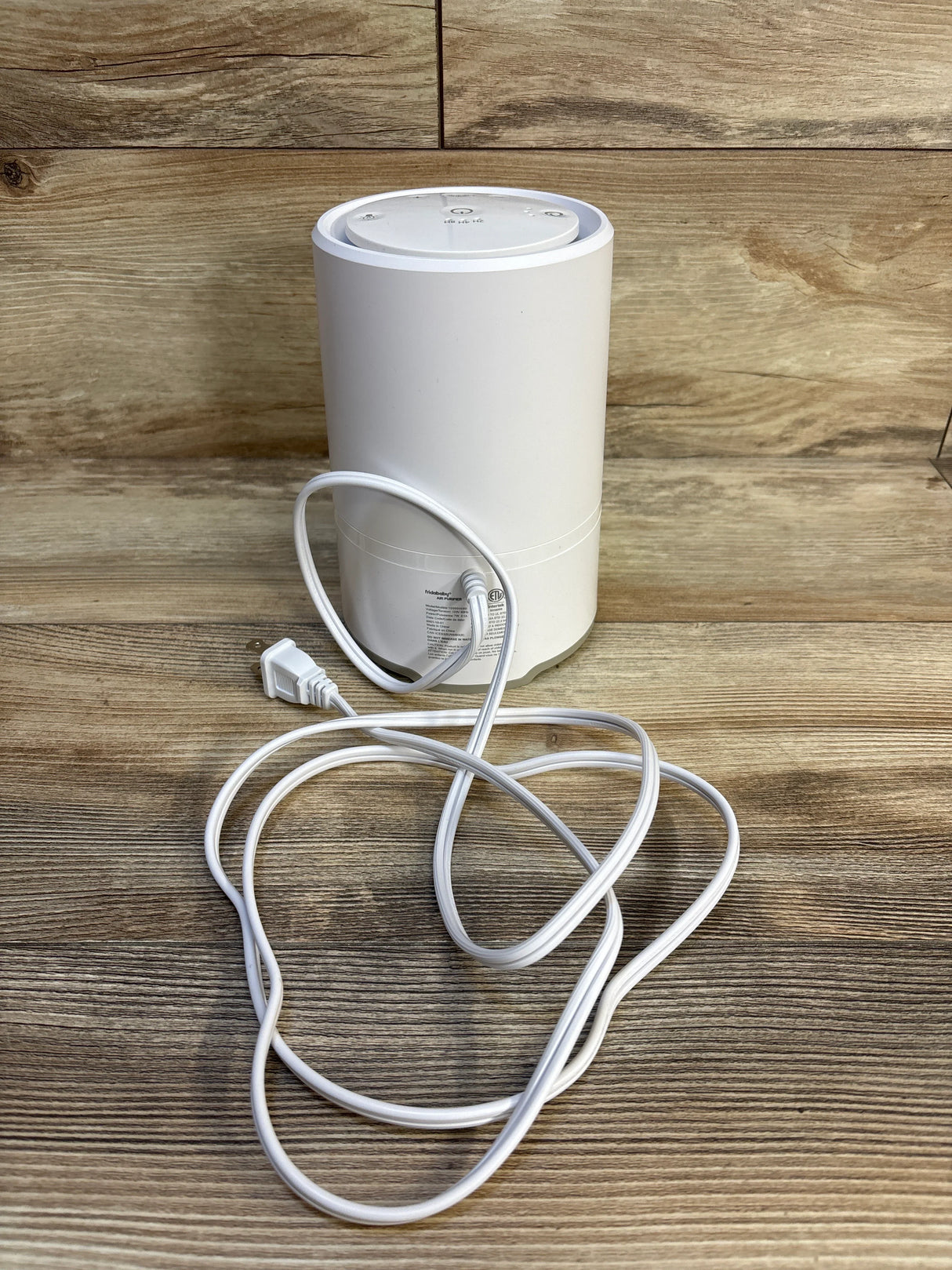 White cylindrical humidifier with power cord on wood surface