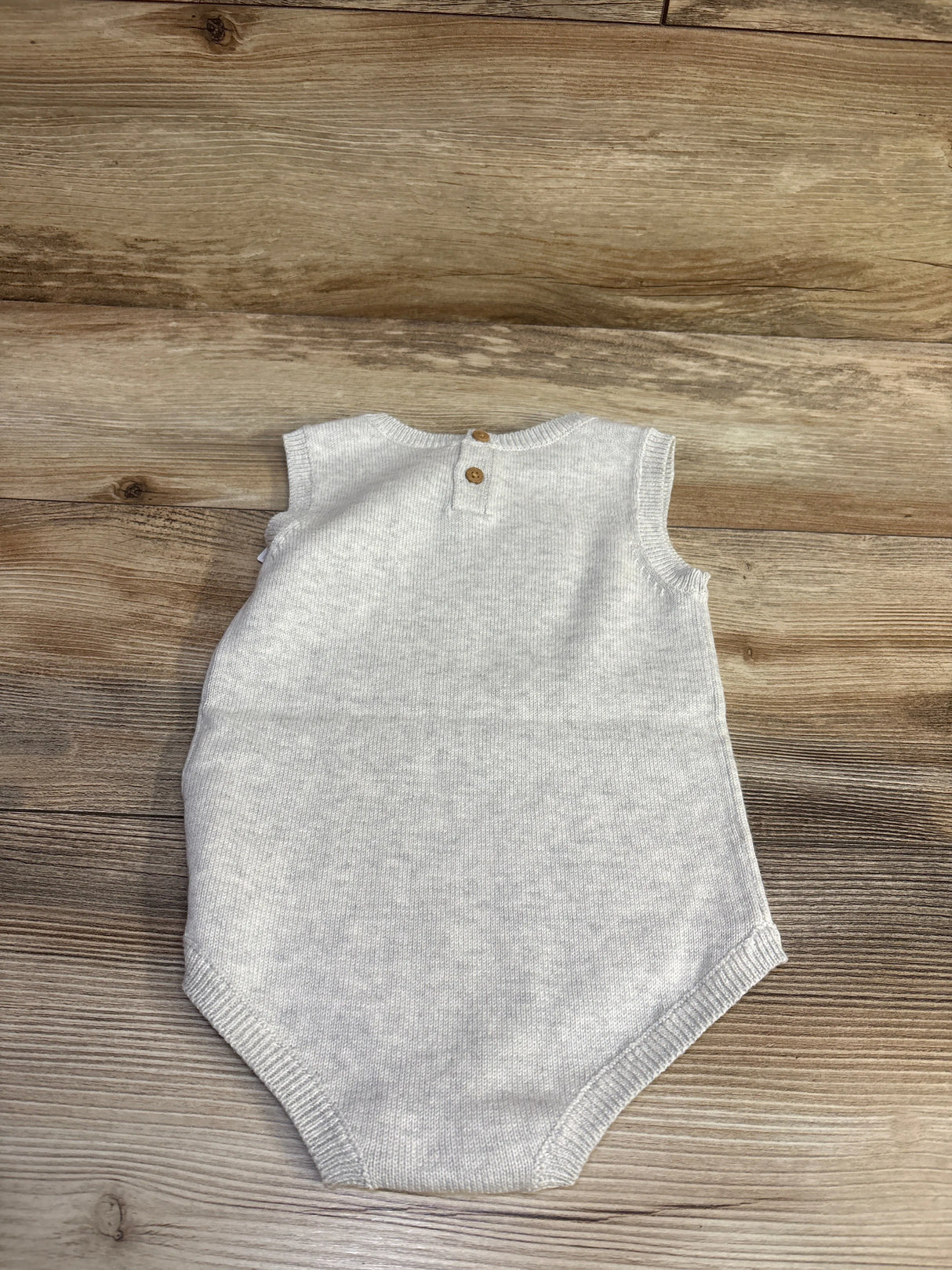Back view of knit baby bubble romper showing two wooden back buttons and ribbed leg openings on wood background