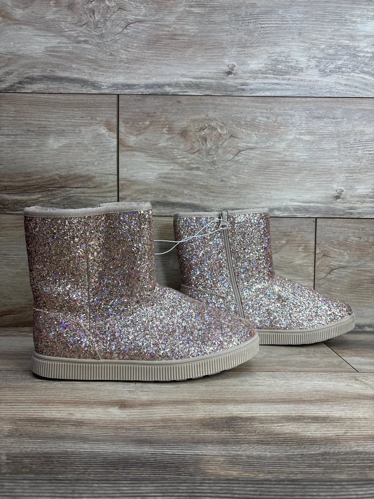 Pair of glittery pink kids boots with zippers on wood background