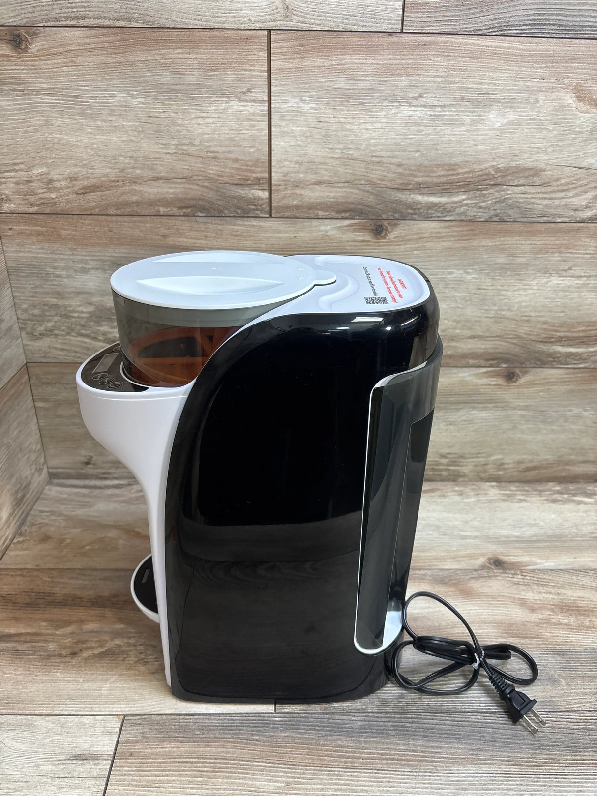 Black and white electric coffee grinder with transparent bean hopper and power cord on wooden surface