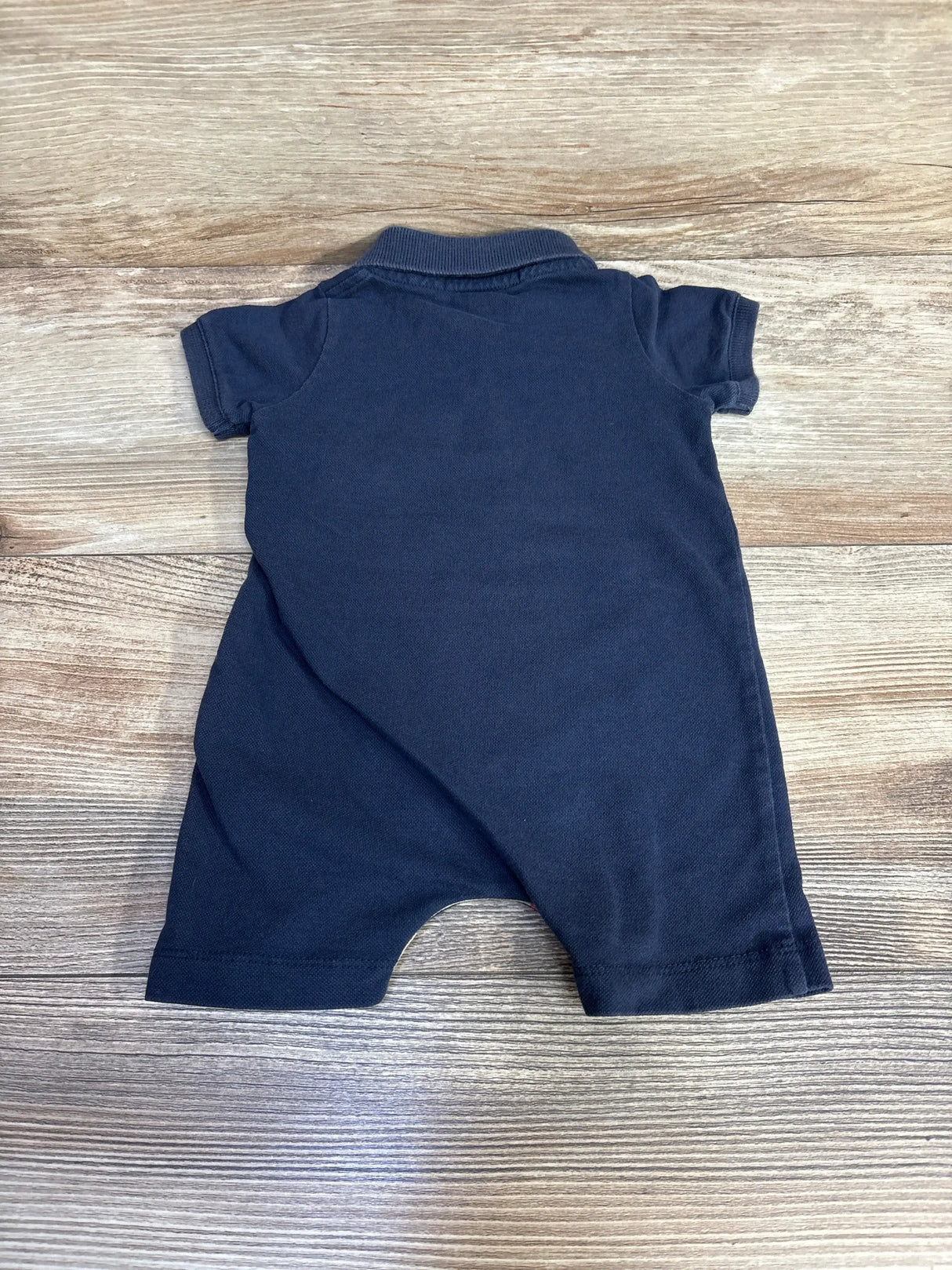 Back view of Burberry navy polo romper, size 3 months, showing short sleeves and ribbed collar on wood background