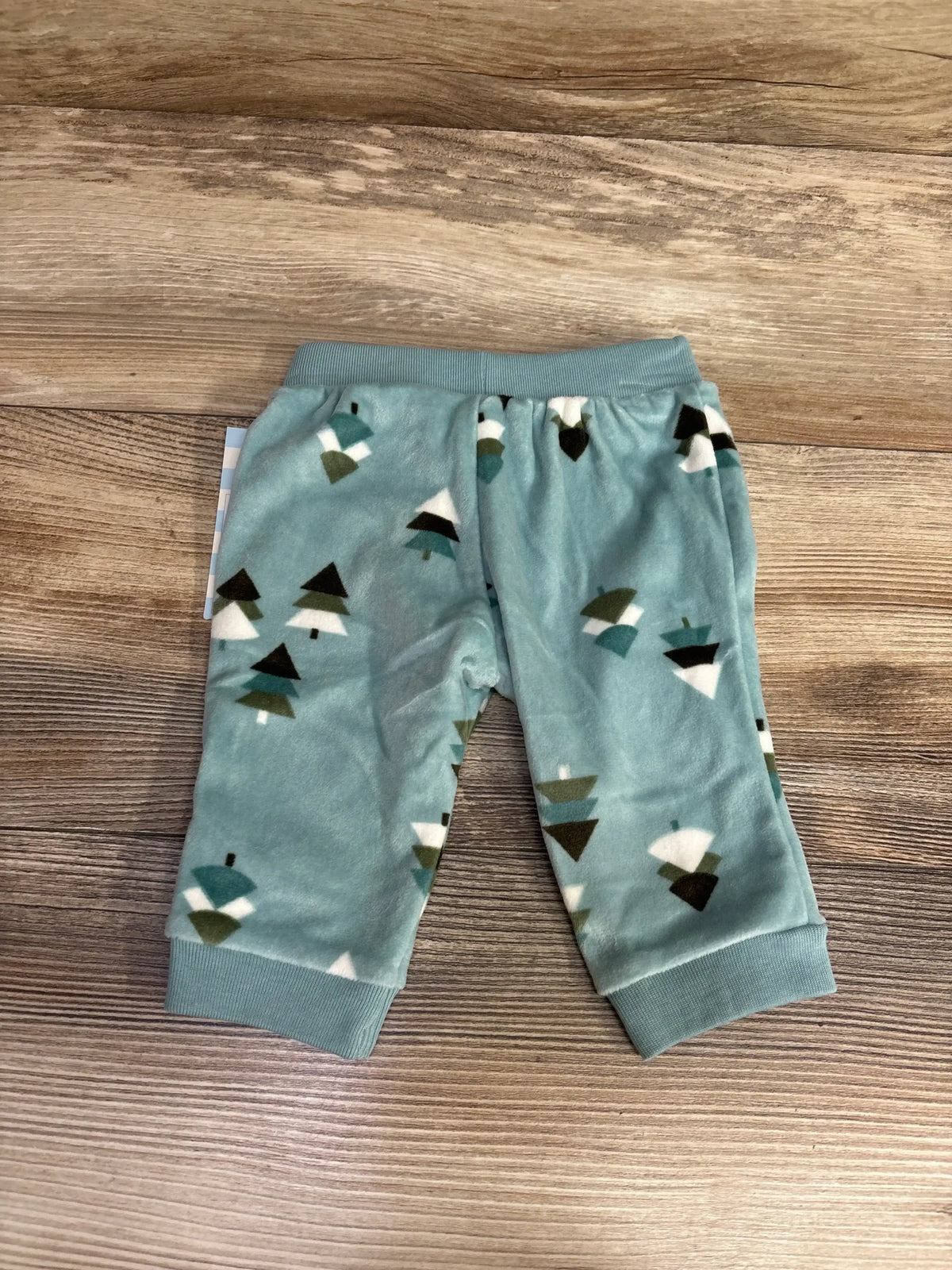 Blue baby pants with green and white tree pattern on wood background, children's clothing