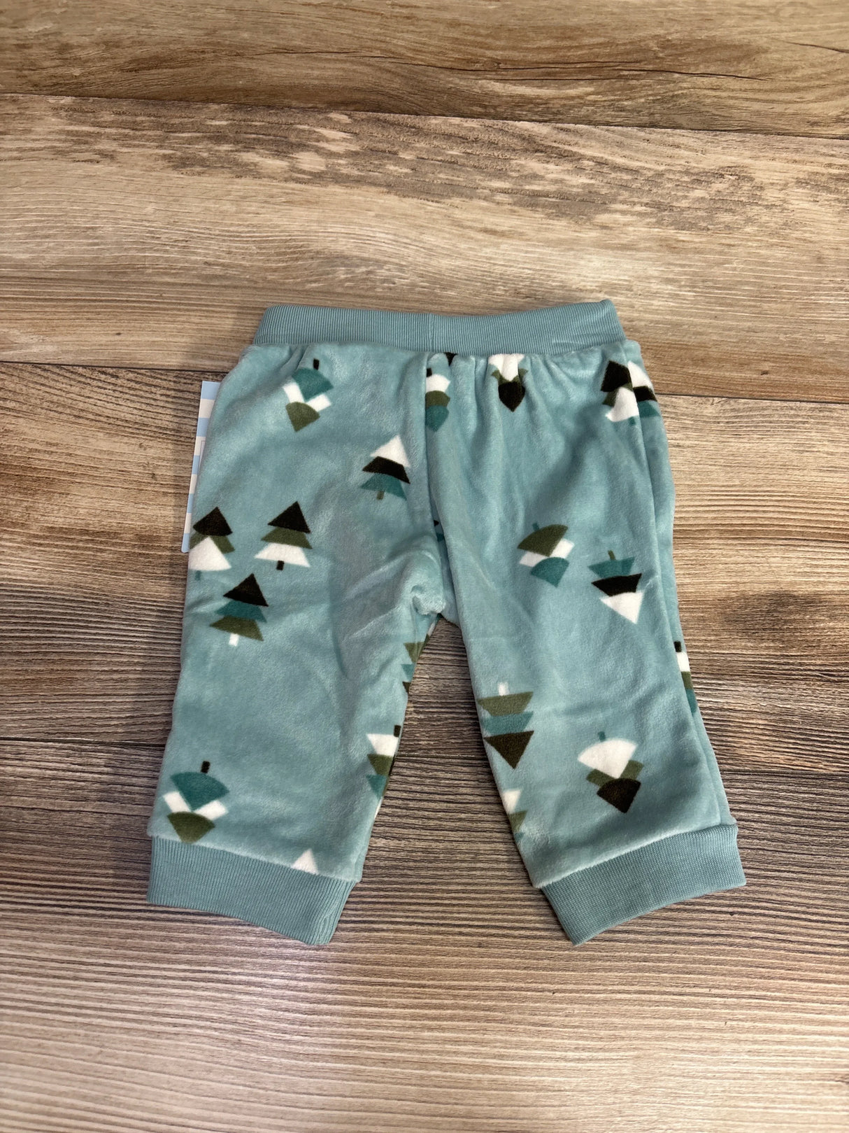 Blue baby pants with green and white tree pattern on wood background, children's clothing