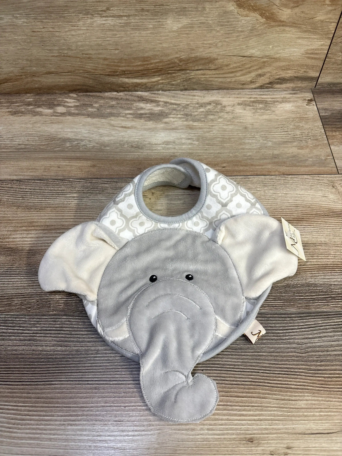 Front view of Emerson elephant bib showing plush grey elephant face and trunk with cream patterned top on wood floor
