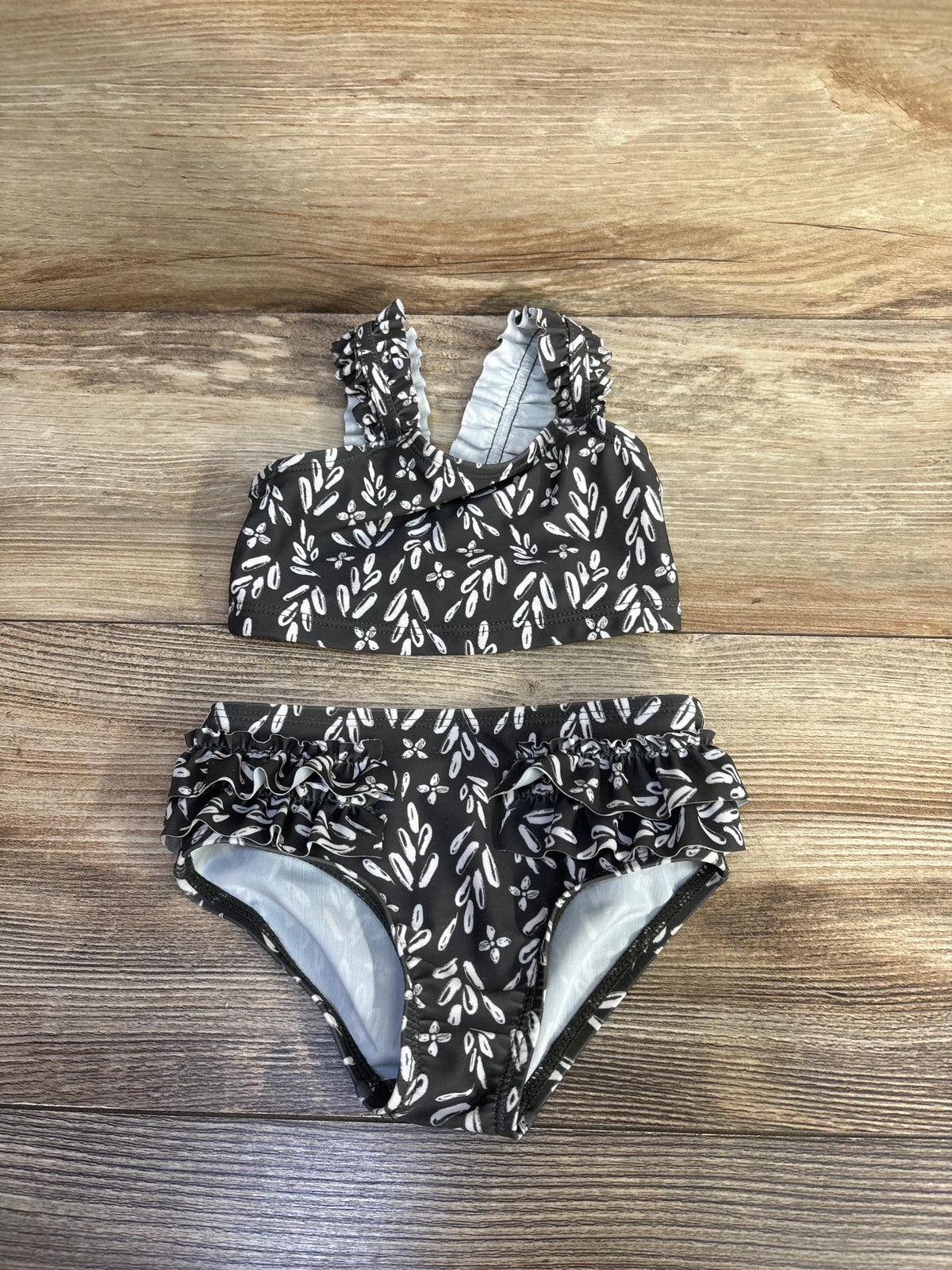 Top down view of Carters two piece ruffle swimsuit set showcasing white floral print and ruffled straps and sides on wood