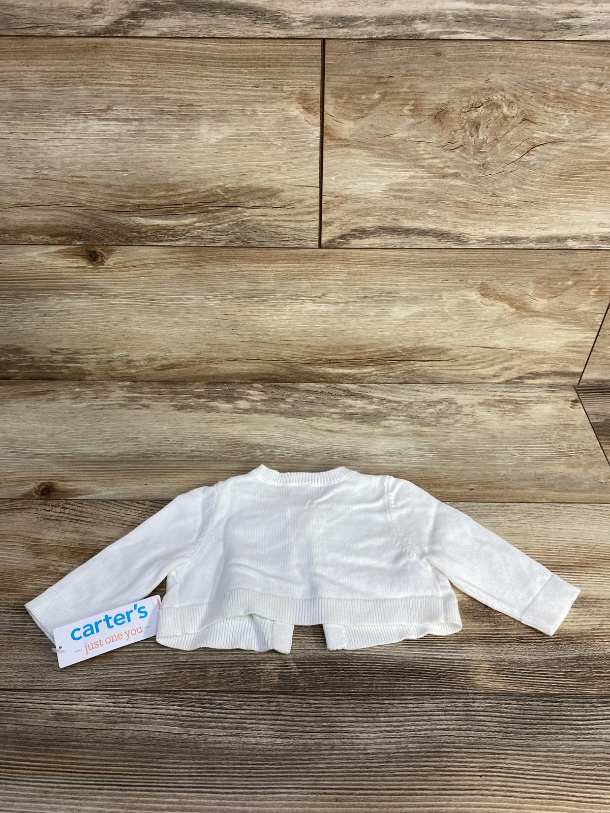 White long-sleeve baby cardigan from Carter's on wooden surface with brand tag attached