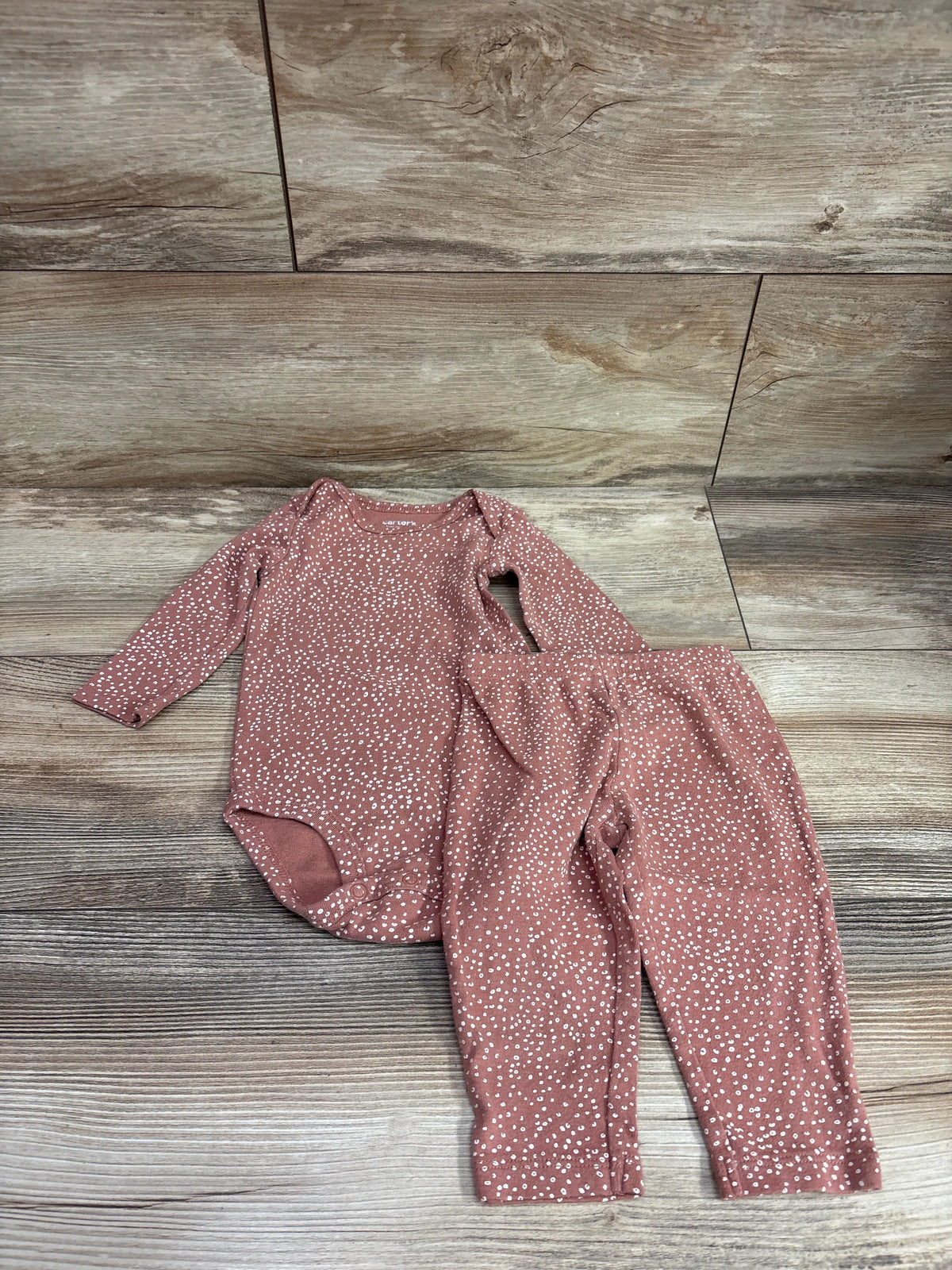 Top-down view of a brown bodysuit and pants set showcasing a white dotted pattern on a wood-look background