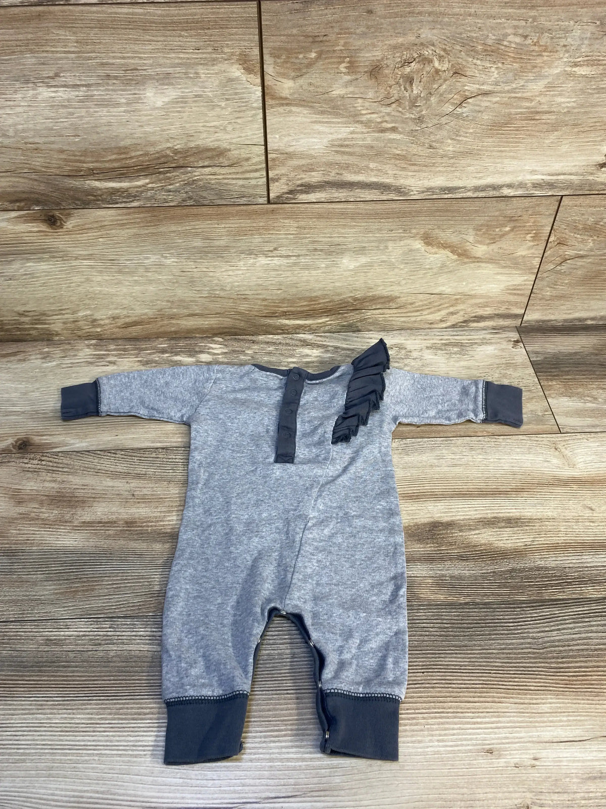 Gray baby romper with dark ruffle detail on chest, laid flat on wood background