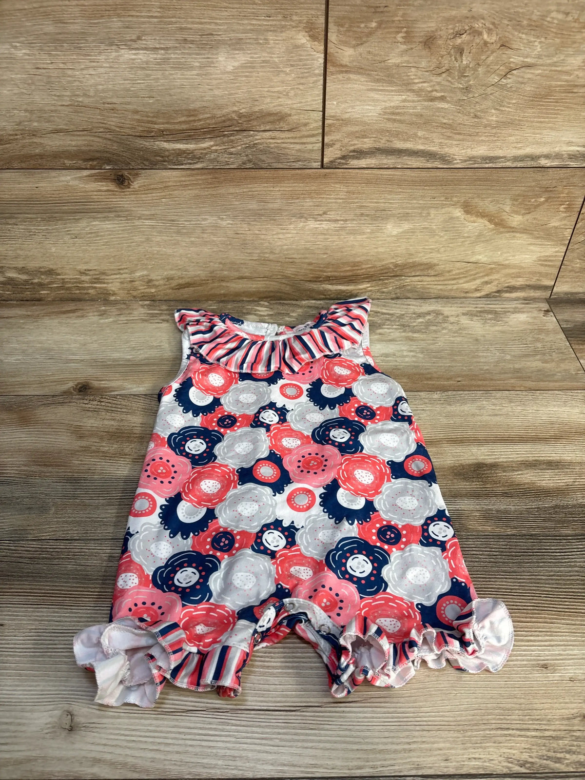 Front view of Pete + Lucy shortie romper in grey showcasing a floral print, ruffled neckline, and ruffled leg openings on wood flooring