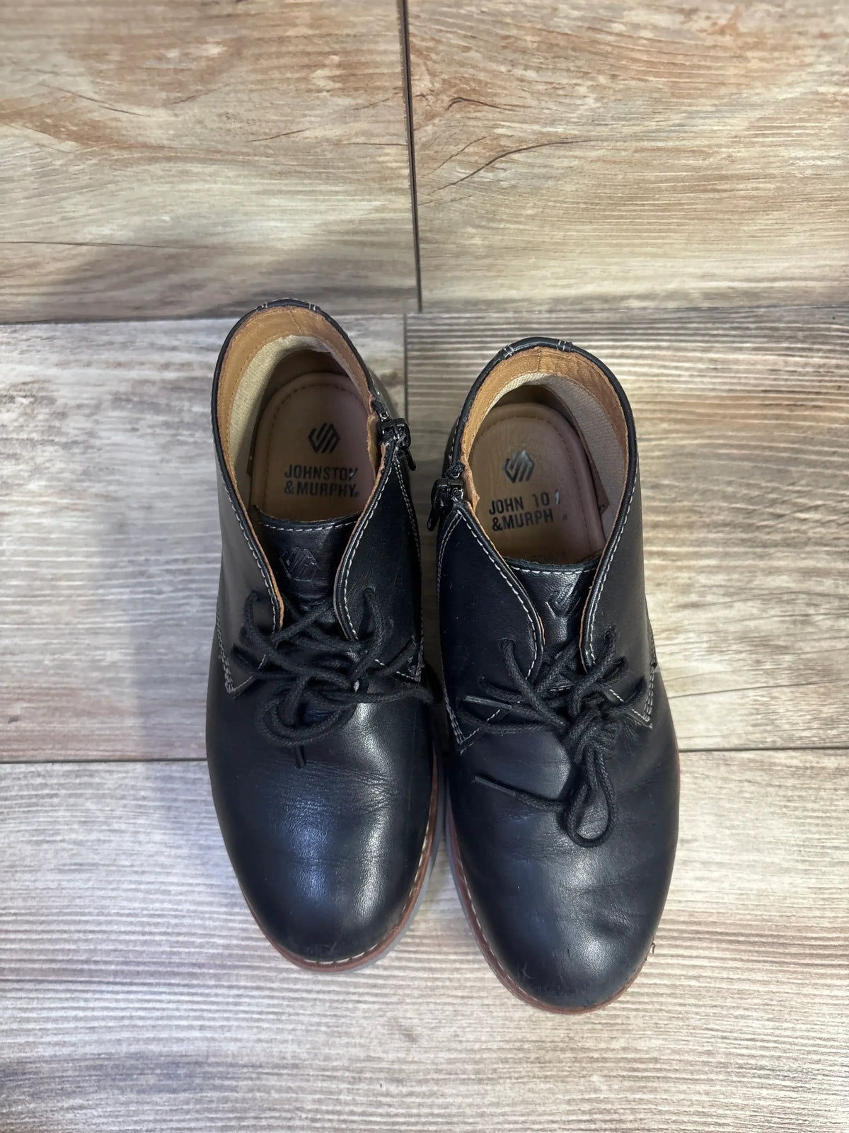 Top-down view of Johnston & Murphy Upton chukka boots showing black leather uppers, lace ties, and light scuffing on wood floor
