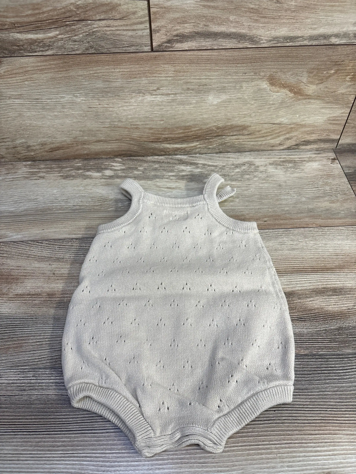 Flat lay of Little Planet organic eyelet bubble romper, tan, 12m, showing eyelet knit texture and bubble silhouette on wood