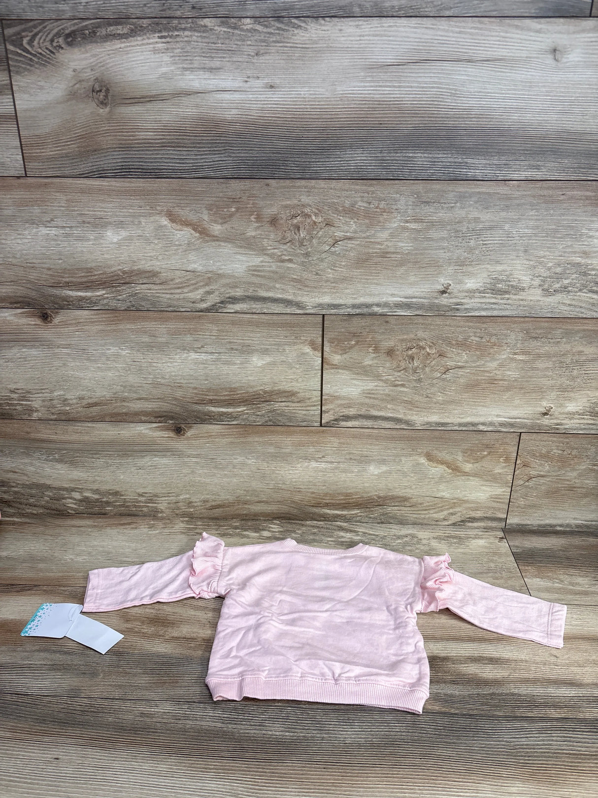 Back view of pink baby sweatshirt showing ruffle long sleeves laid flat on wood floor