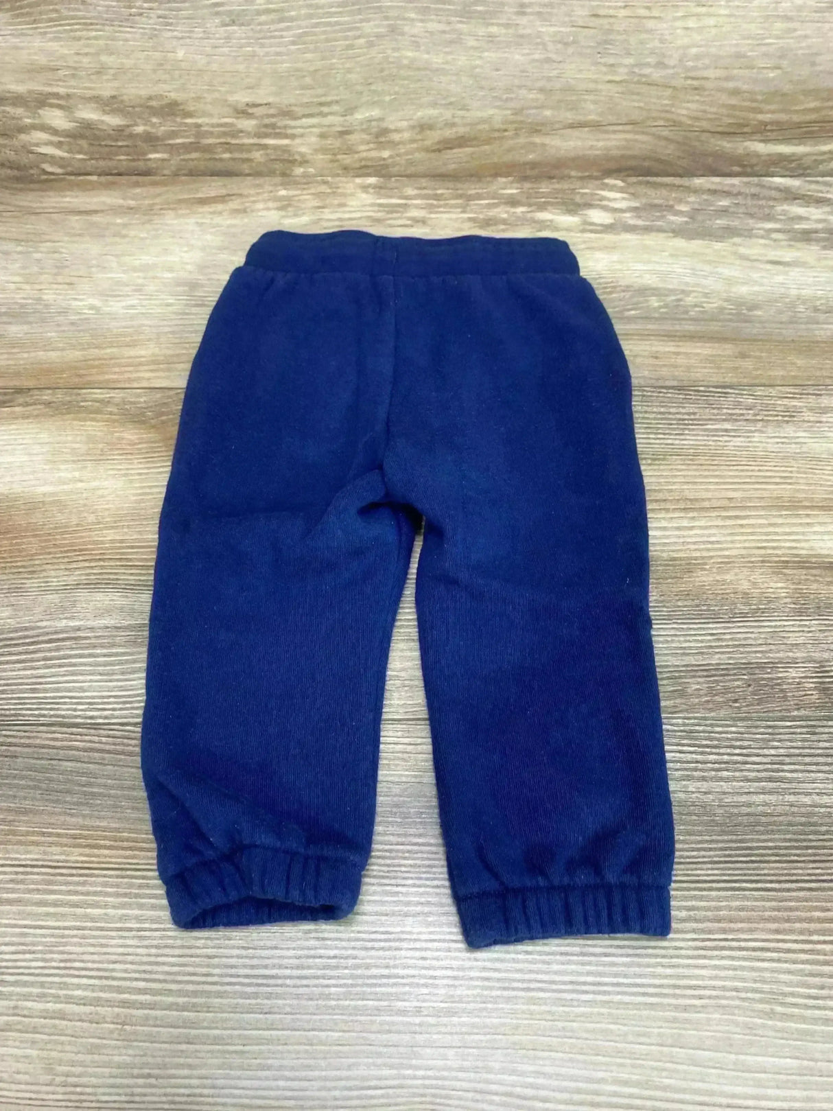 Flat lay of Okie Dokie drawstring joggers in navy fleece with elastic cuffs on wood plank background
