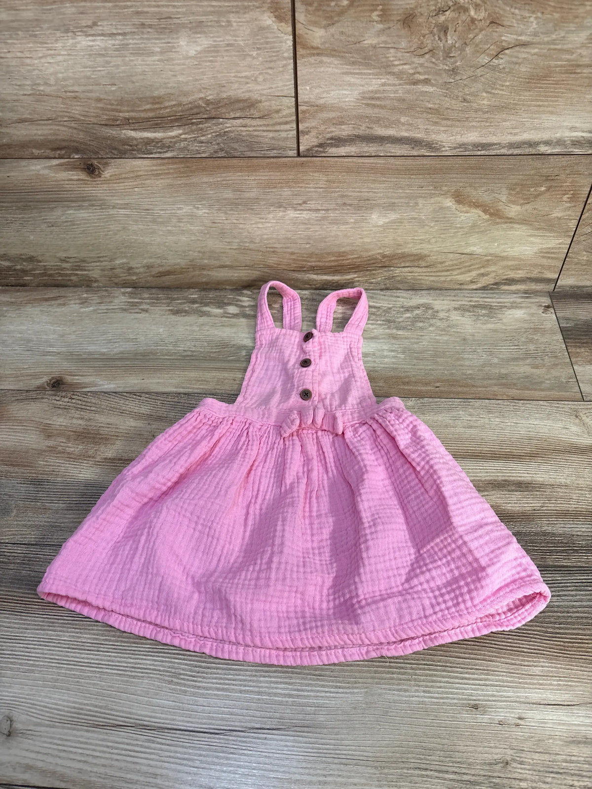 Front view of Young Hearts gauze skirtall showcasing pink gathered skirt, buttoned bib, and shoulder straps on a wood-grain background