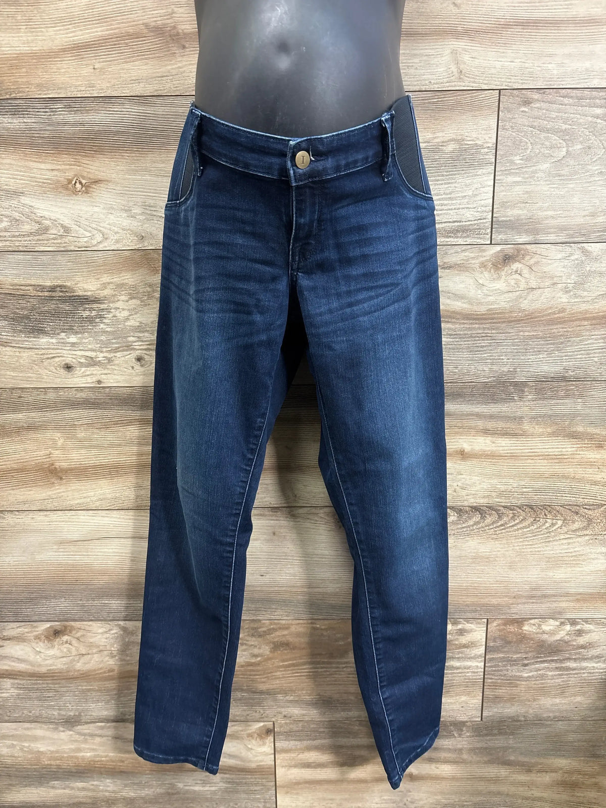Front view of navy Isabel maternity skinny jeans showing elastic side panels and faded whiskering on a torso mannequin against wood plank background
