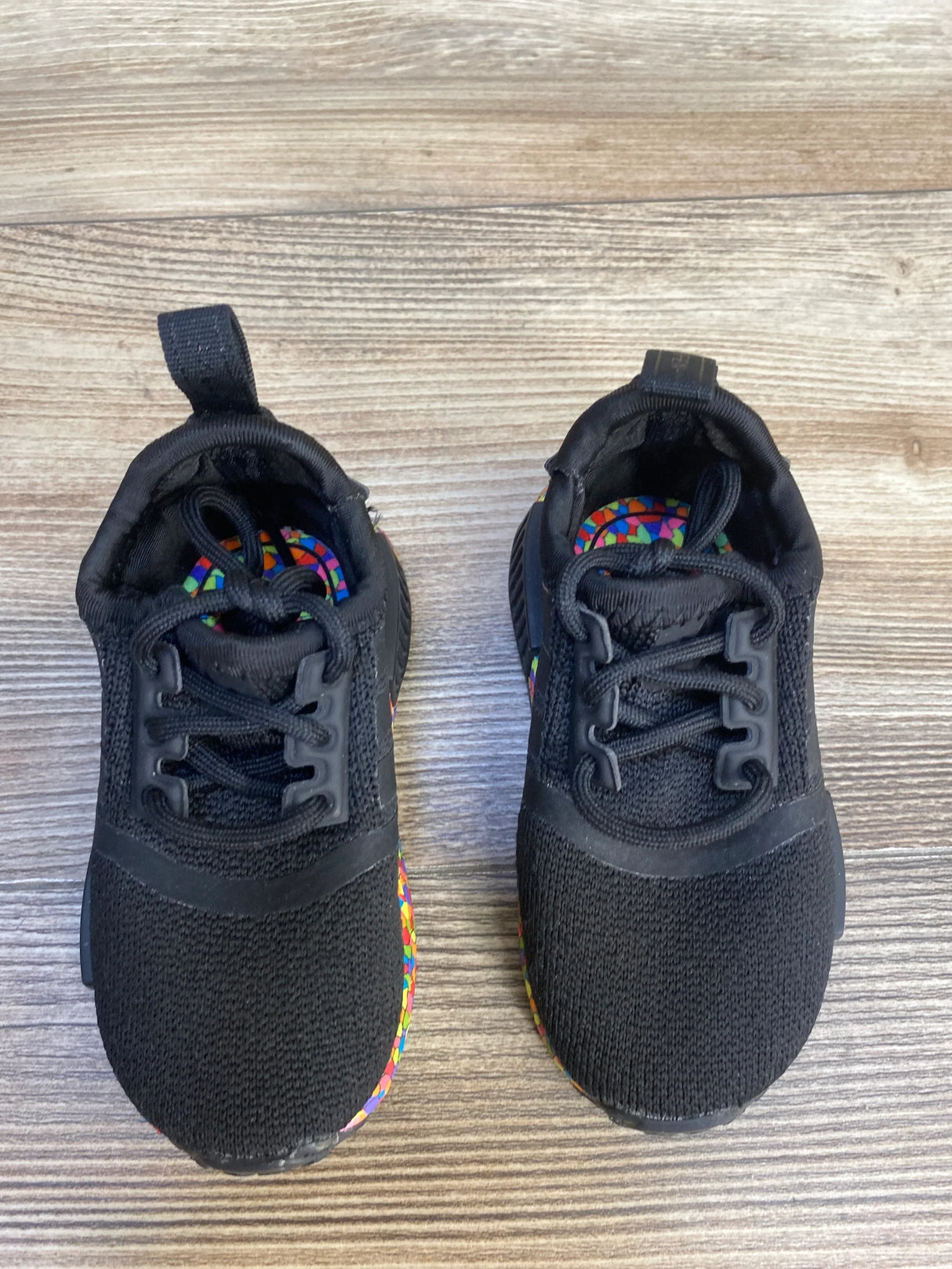 Black toddler sneakers with colorful patterned insoles on wood floor