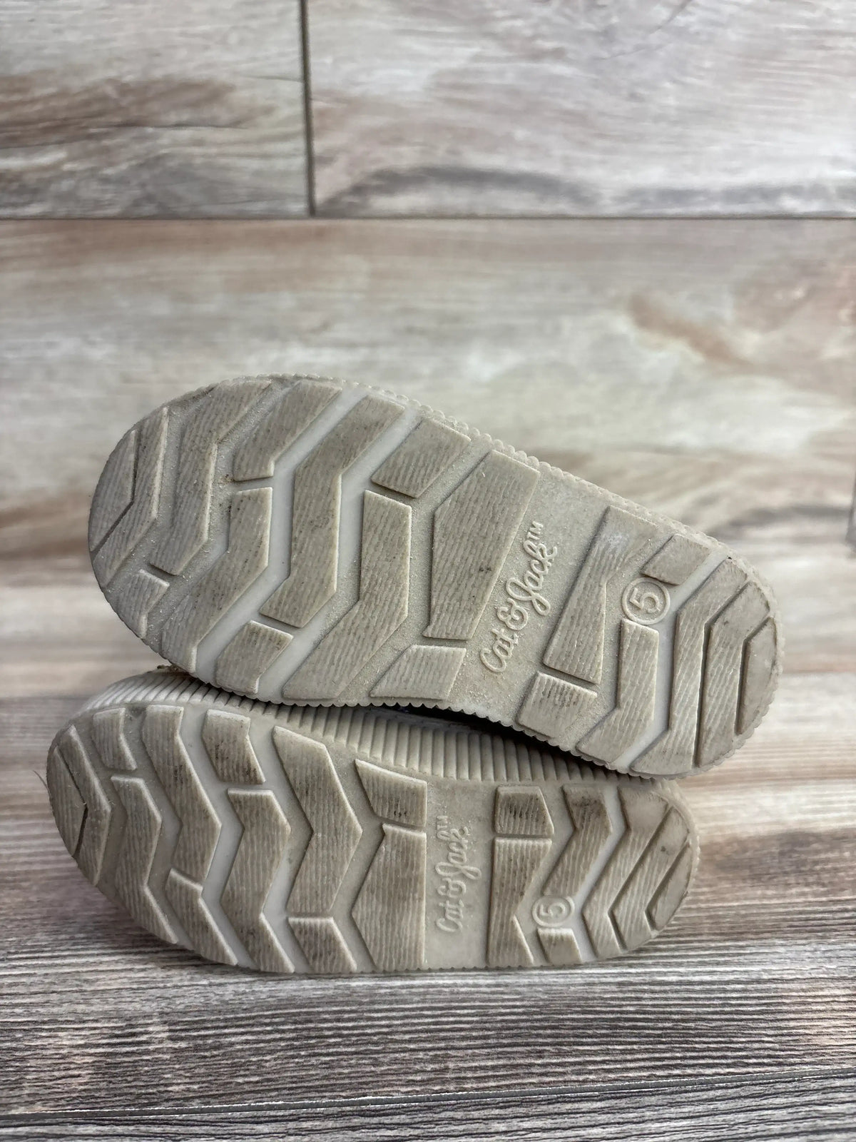 Bottom view of used Cat & Jack kids shoes size 5 with tread pattern on wooden floor