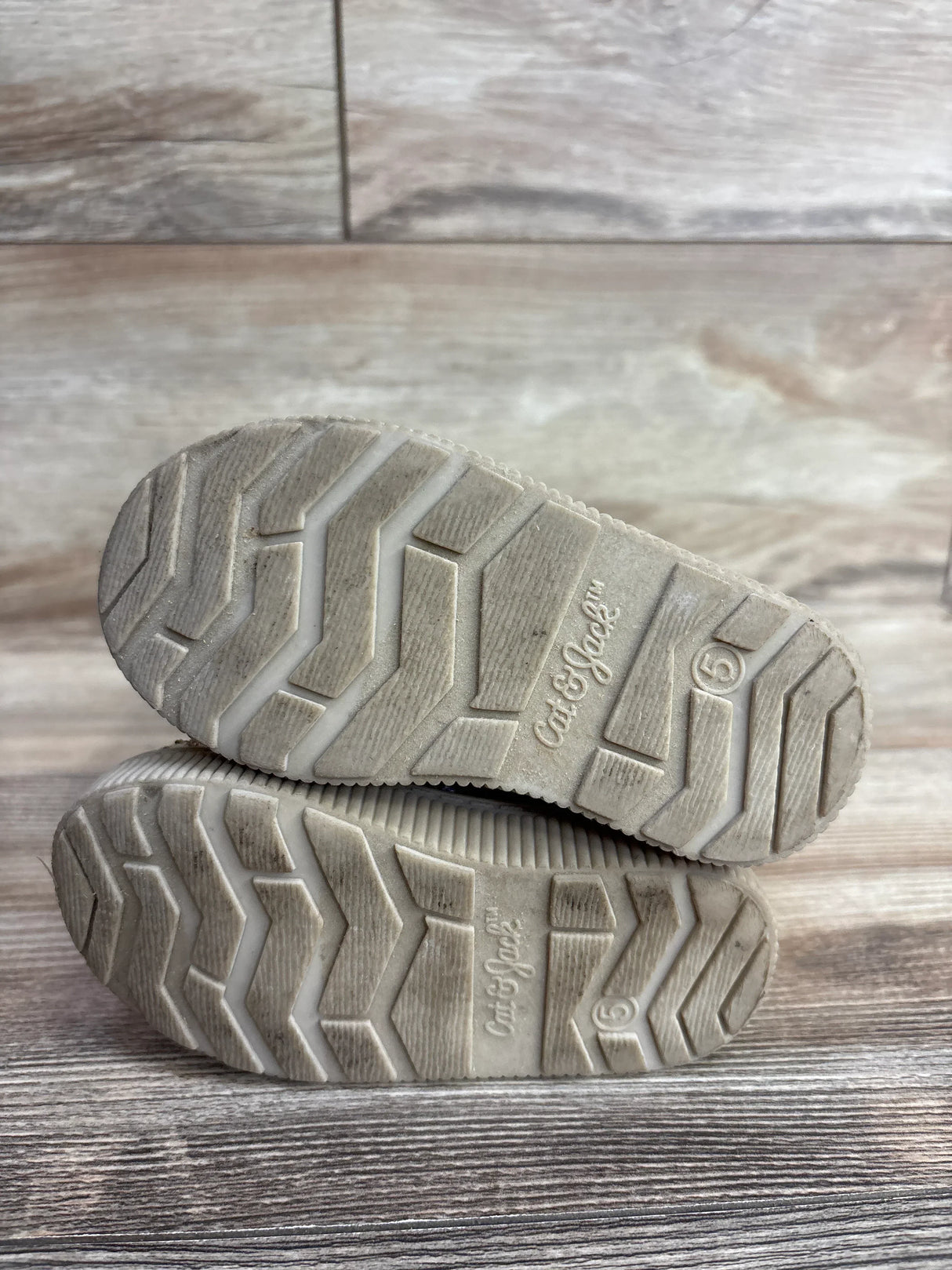 Bottom view of used Cat & Jack kids shoes size 5 with tread pattern on wooden floor
