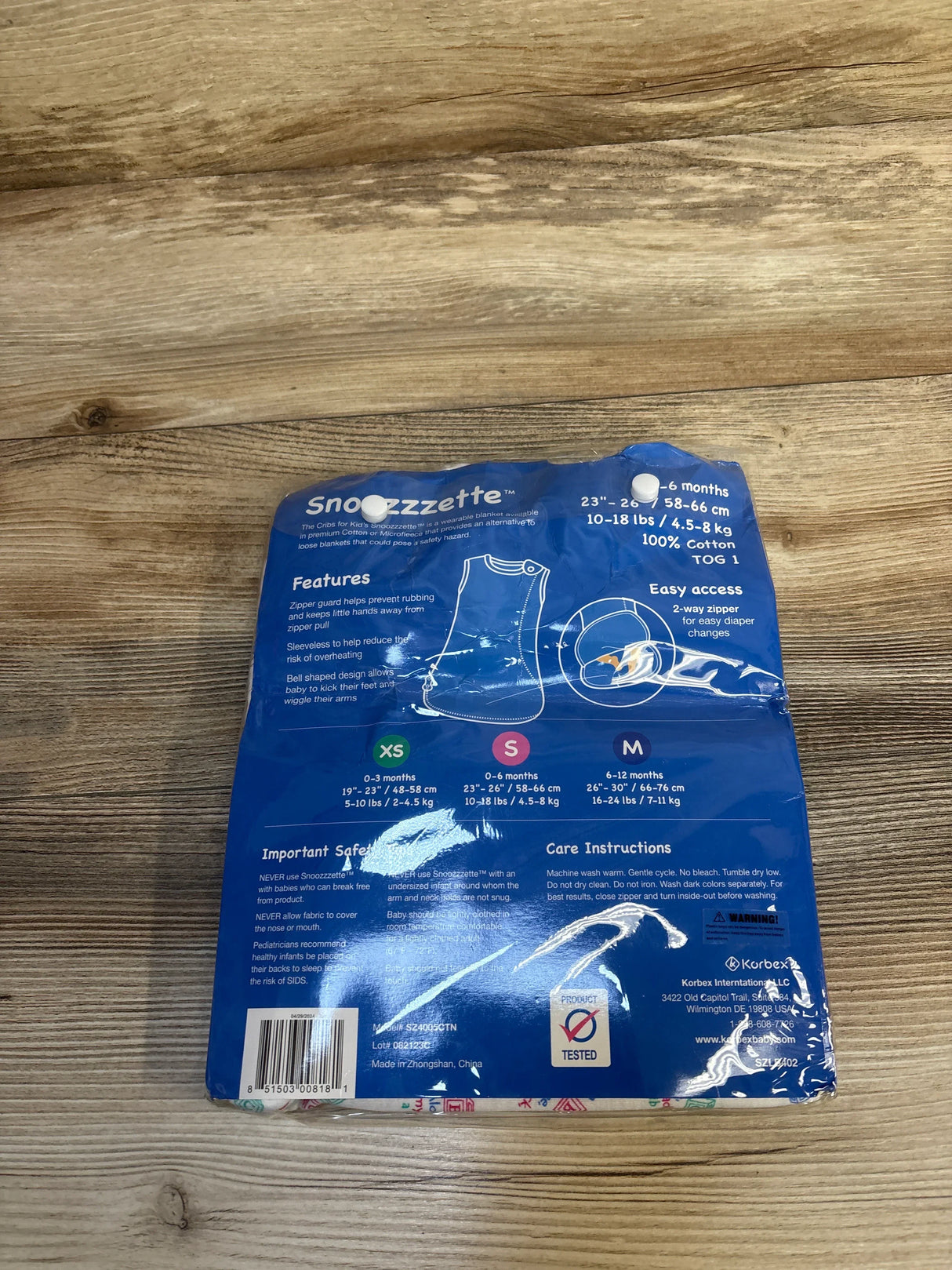 Blue Snoozzzette wearable blanket packaging for infants on wood background with size chart visible.