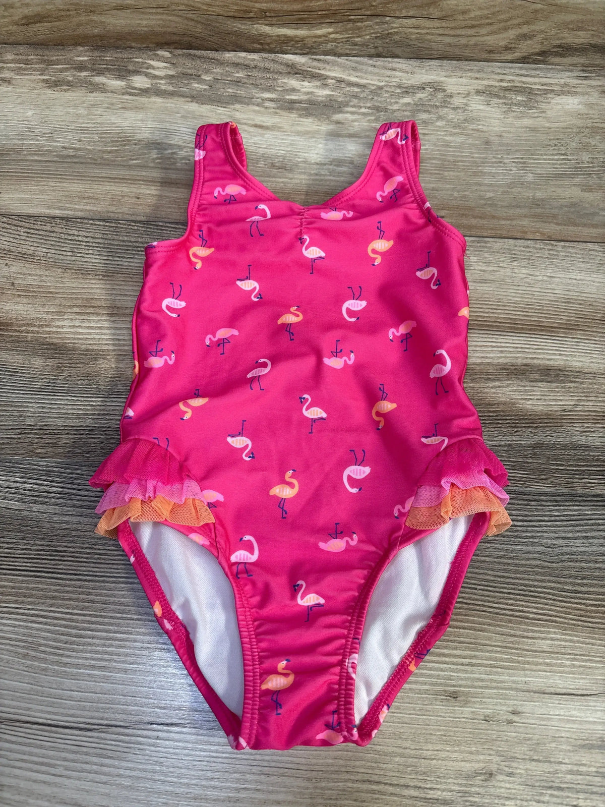 Front view of toddler one-piece flamingo print swimsuit with pink tulle ruffle trim on wood background