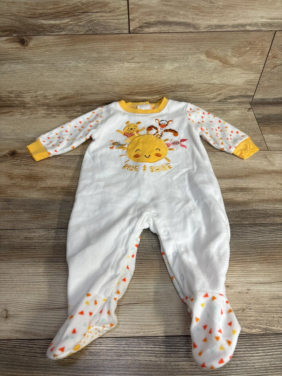 White baby sleeper with colorful print, Rise & Shine sun, and animal characters on wood floor
