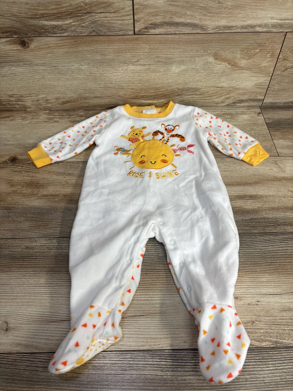 White baby sleeper with colorful print, Rise & Shine sun, and animal characters on wood floor