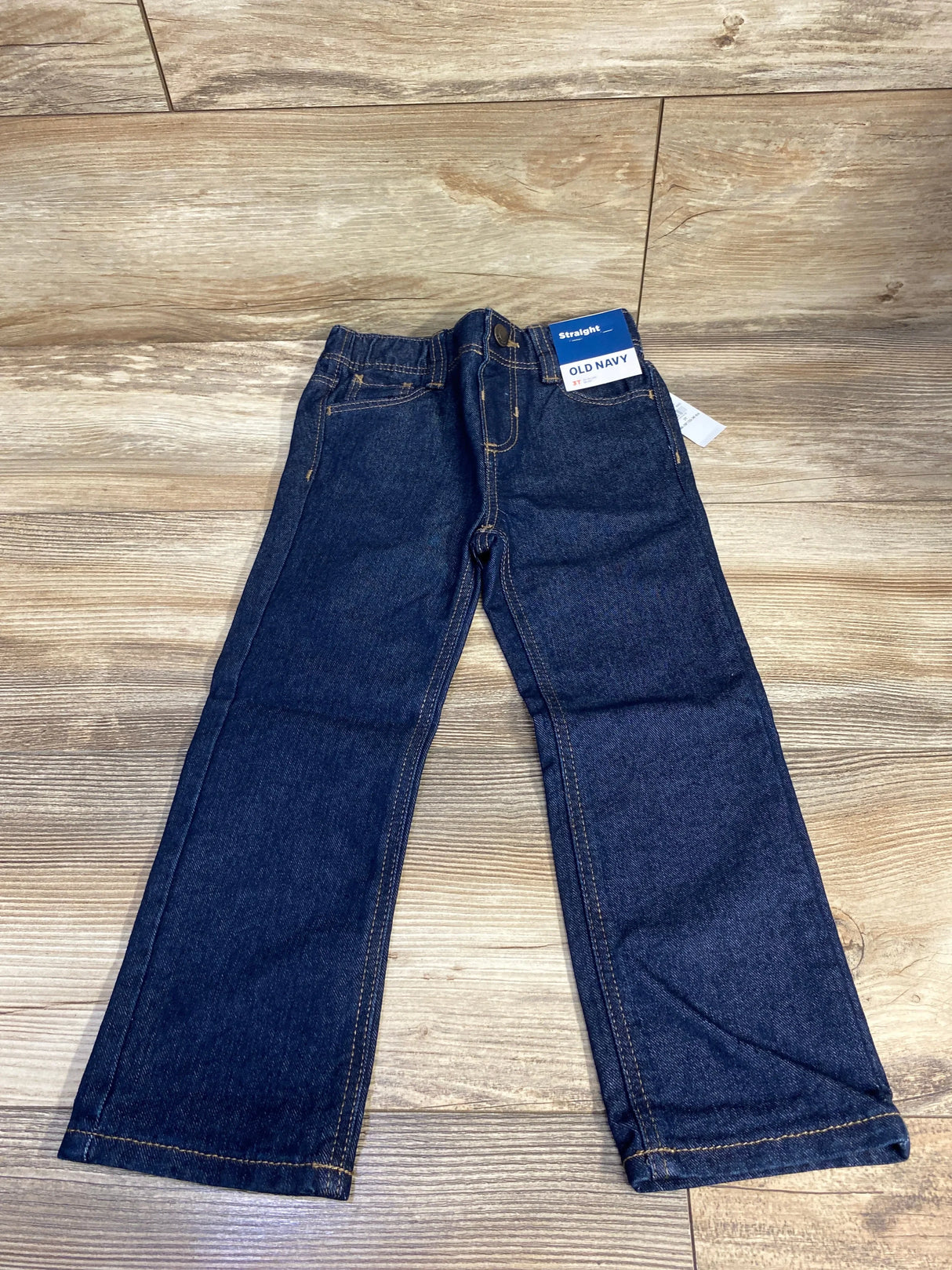 Kids dark wash straight leg jeans with yellow stitching on wood floor