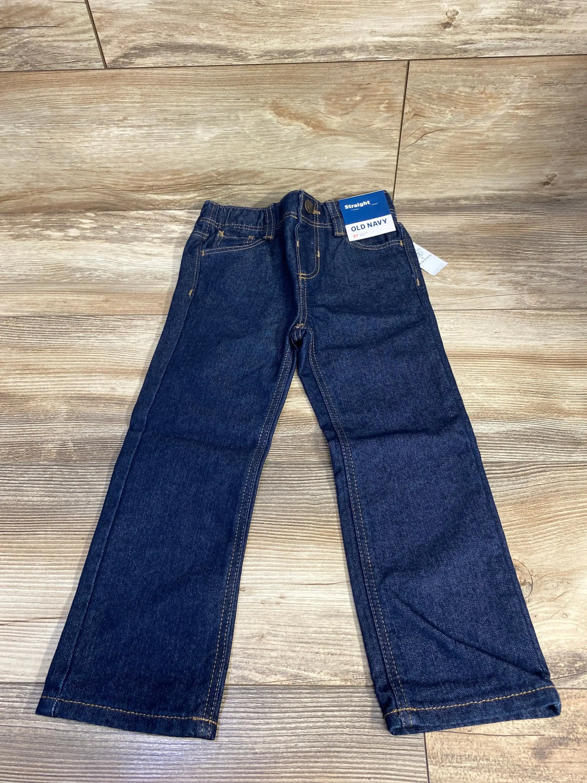 Kids dark wash straight leg jeans with yellow stitching on wood floor
