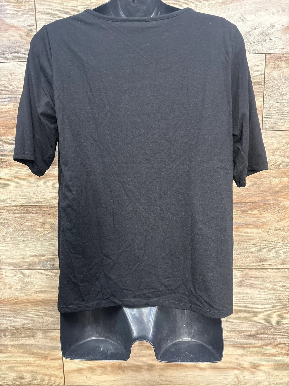 Plain black short-sleeve t-shirt displayed on partial black mannequin torso against wood plank background