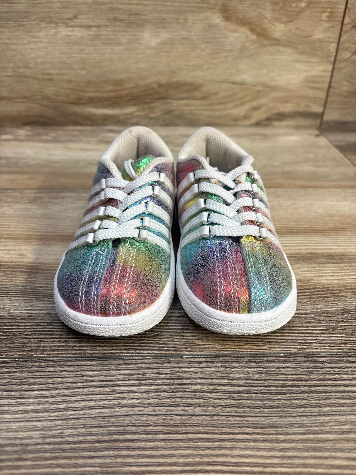 Front view of K-Swiss Classic VN toddler sneakers size 7C showing rainbow metallic glitter upper, white laces and white sole on wood background