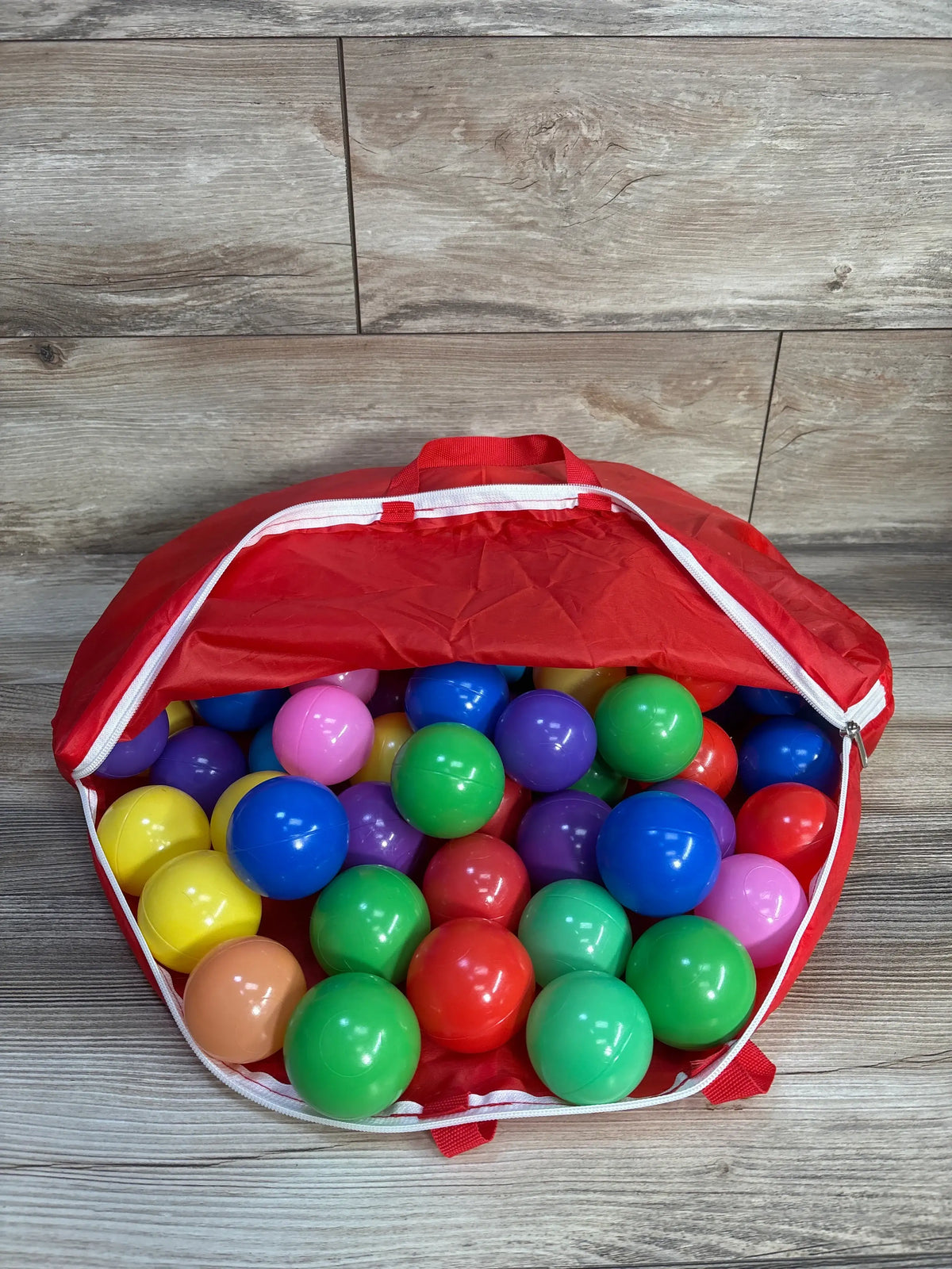 Open bag of Bestway Multicolor Plastic Ball Pit Balls showcasing multicolor plastic balls and a red storage bag on a wood floor