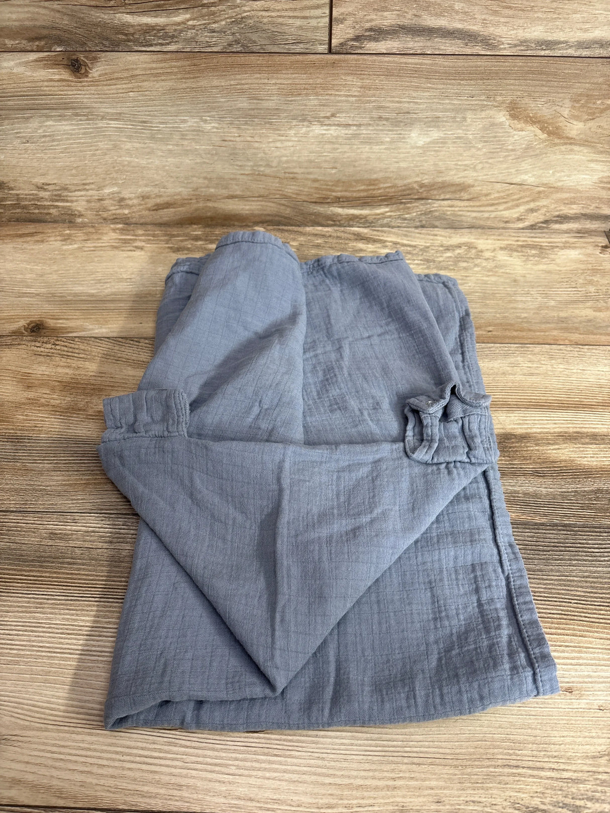 Top-down view of Comfy Cubs muslin car seat cover folded to show soft crinkled texture and elastic strap on wood background