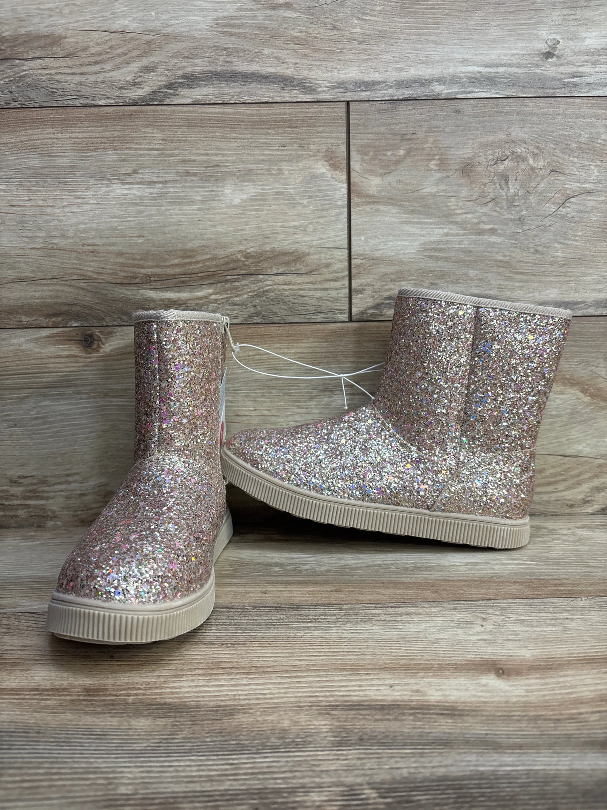 Sparkly pink glitter kids boots with rubber soles on a wooden background