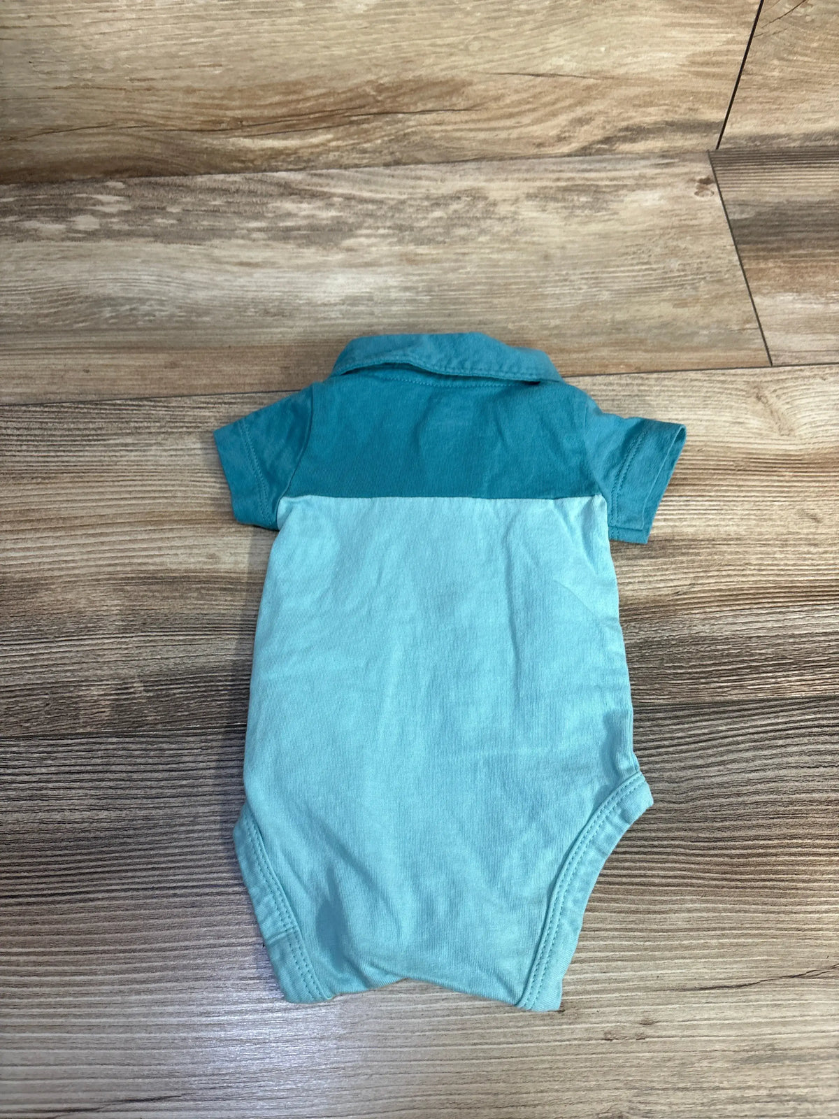 Back view of a blue Carter’s newborn polo bodysuit showcasing its collar and short sleeves on a wood-grain floor