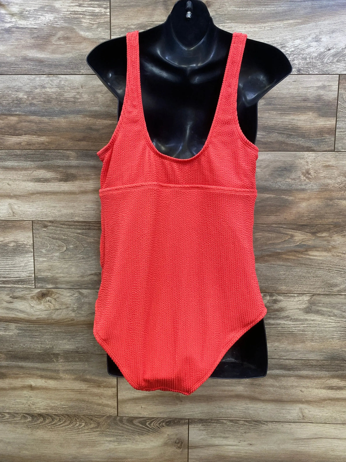 Front view of red maternity one piece swimsuit on black torso showing scoop neckline and textured fabric on wood background