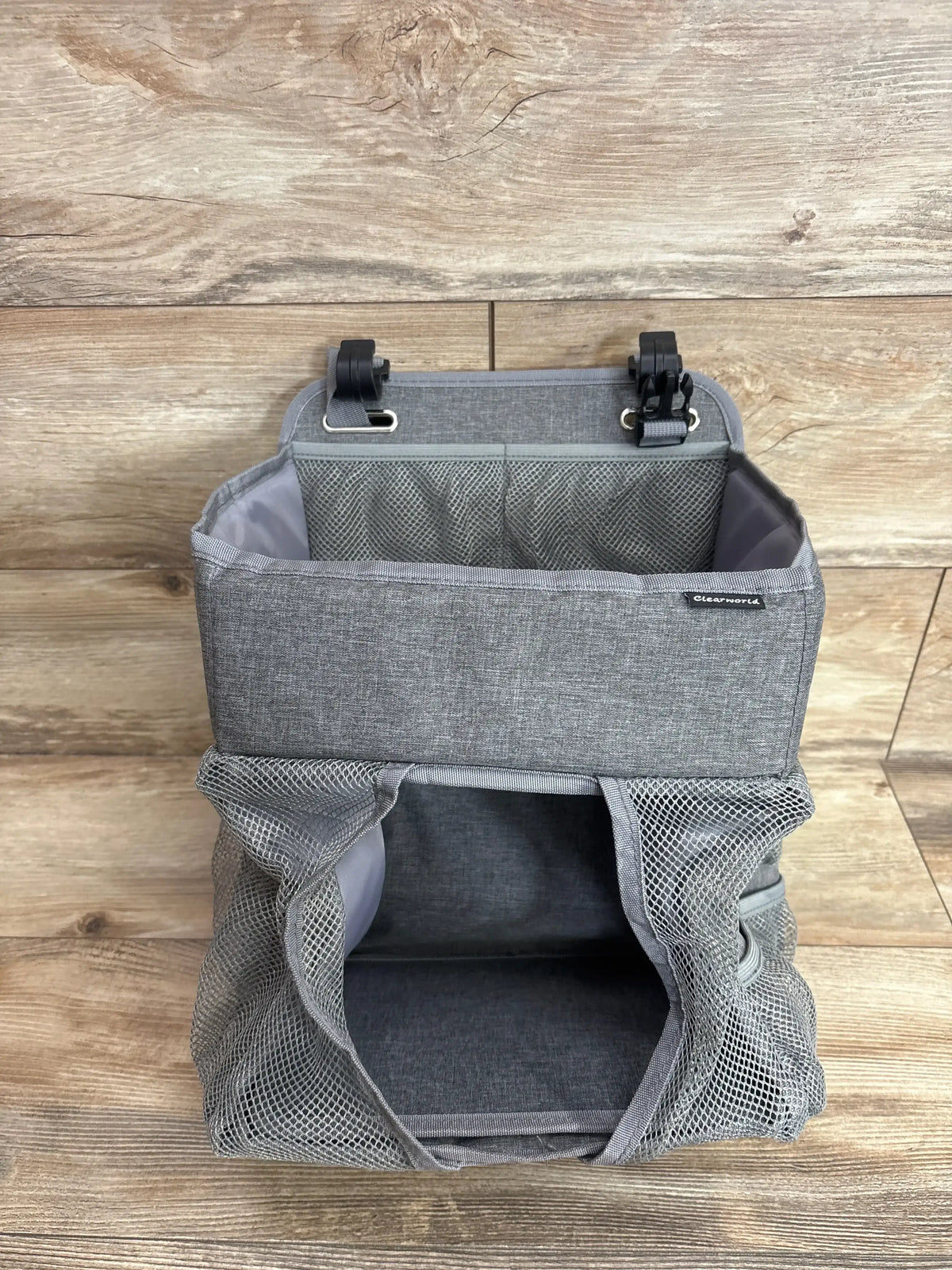 Front view of ClearWorld hanging diaper caddy showcasing open main compartment, mesh side pockets, and mounting clips against wood background