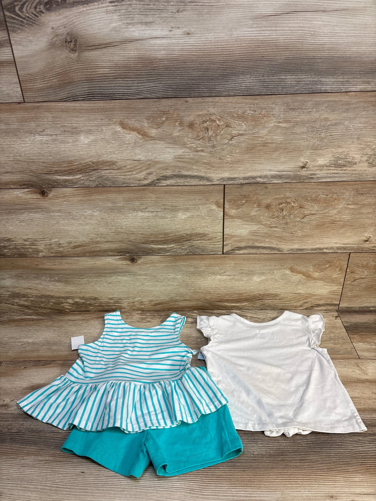 Toddler girl's striped peplum top with teal shorts and white ruffle-sleeve shirt on wood floor